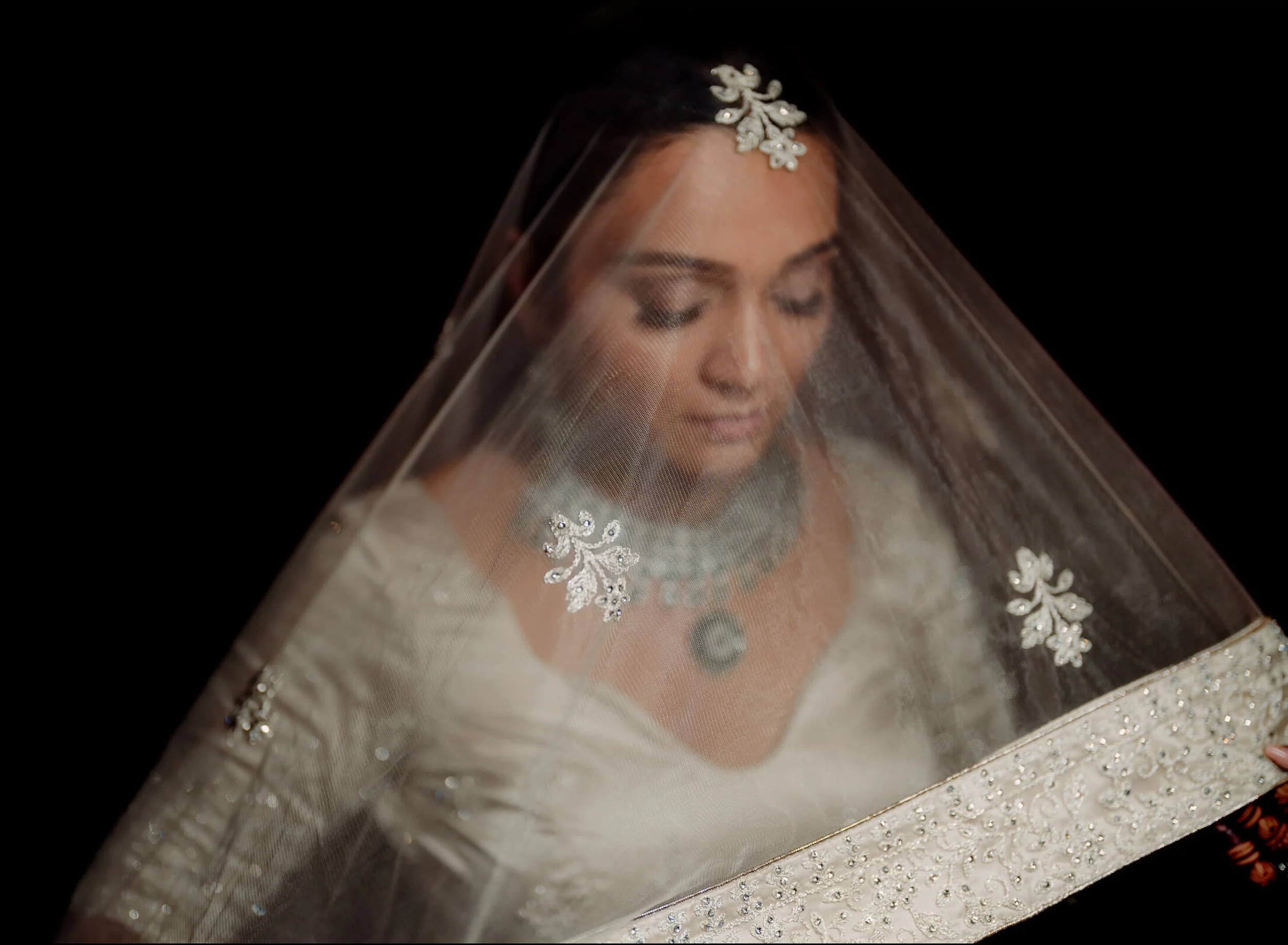 Close-up of a woman's face on a portrait picture inside a decorative metallic box with floral embellishments, with a black background.