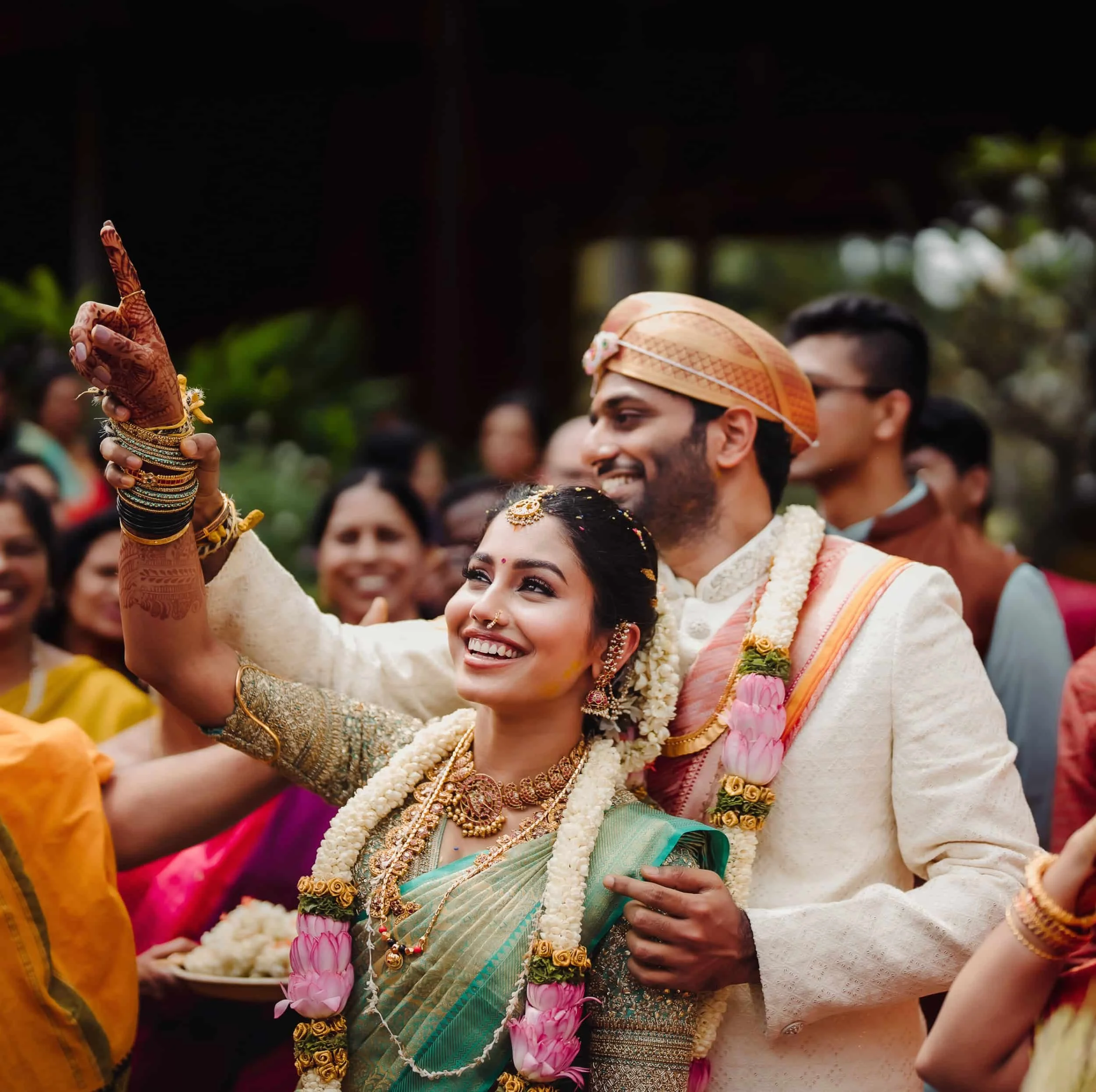A wedding celebration with Indian traditional attire, including a bride and groom, surrounded by guests, with jewelry, flowers, and cultural decorations.