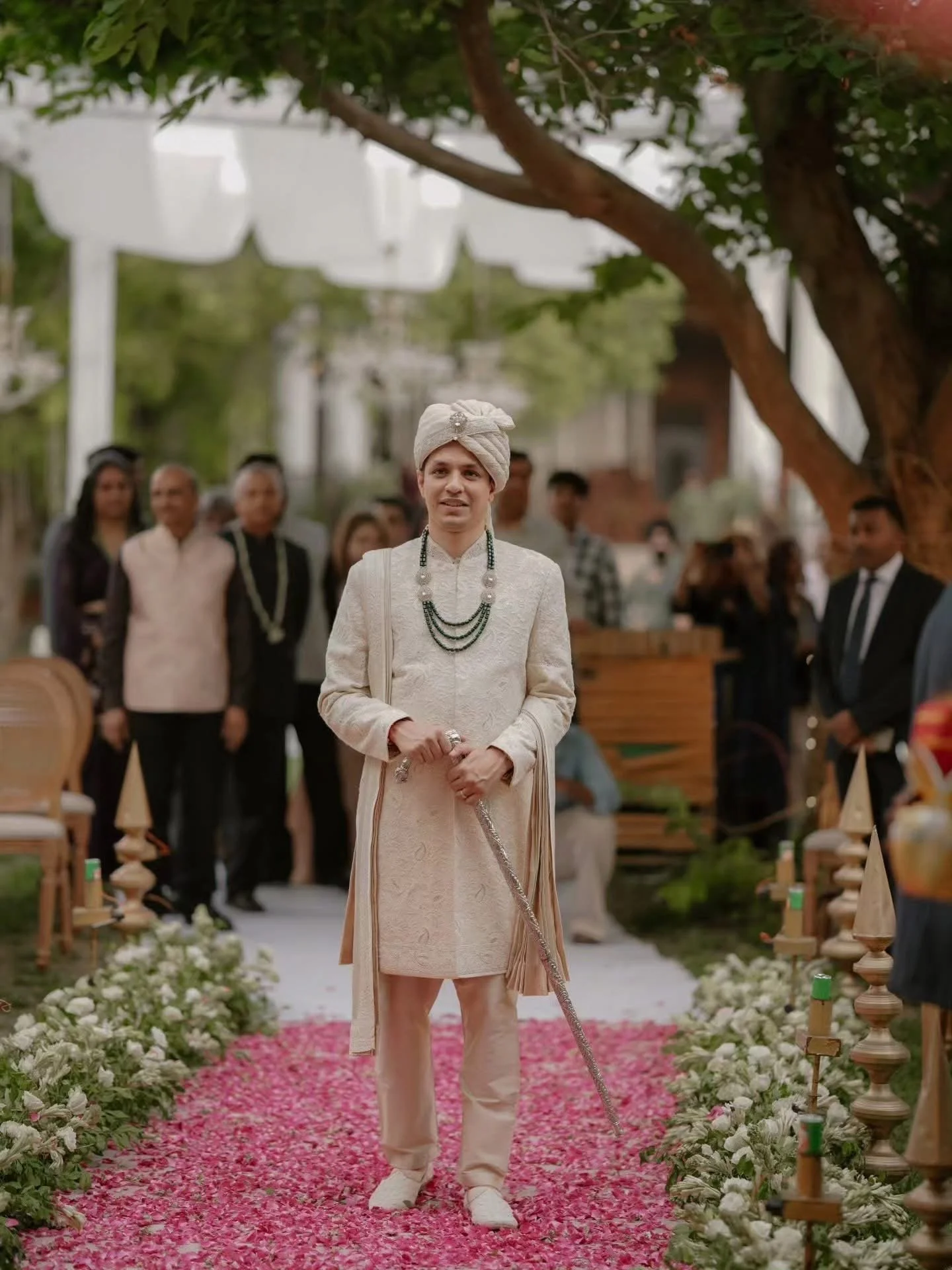 Person in traditional attire standing on an aisle decorated with pink and white flower petals during a cultural or wedding ceremony.