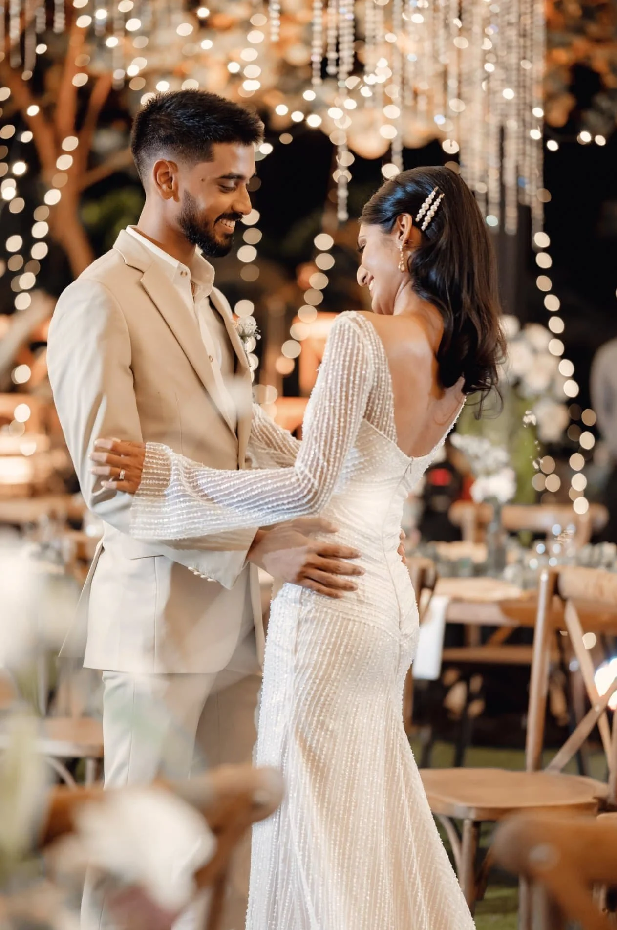 A couple dancing at a wedding reception, with fairy lights and hanging decorations in the background.