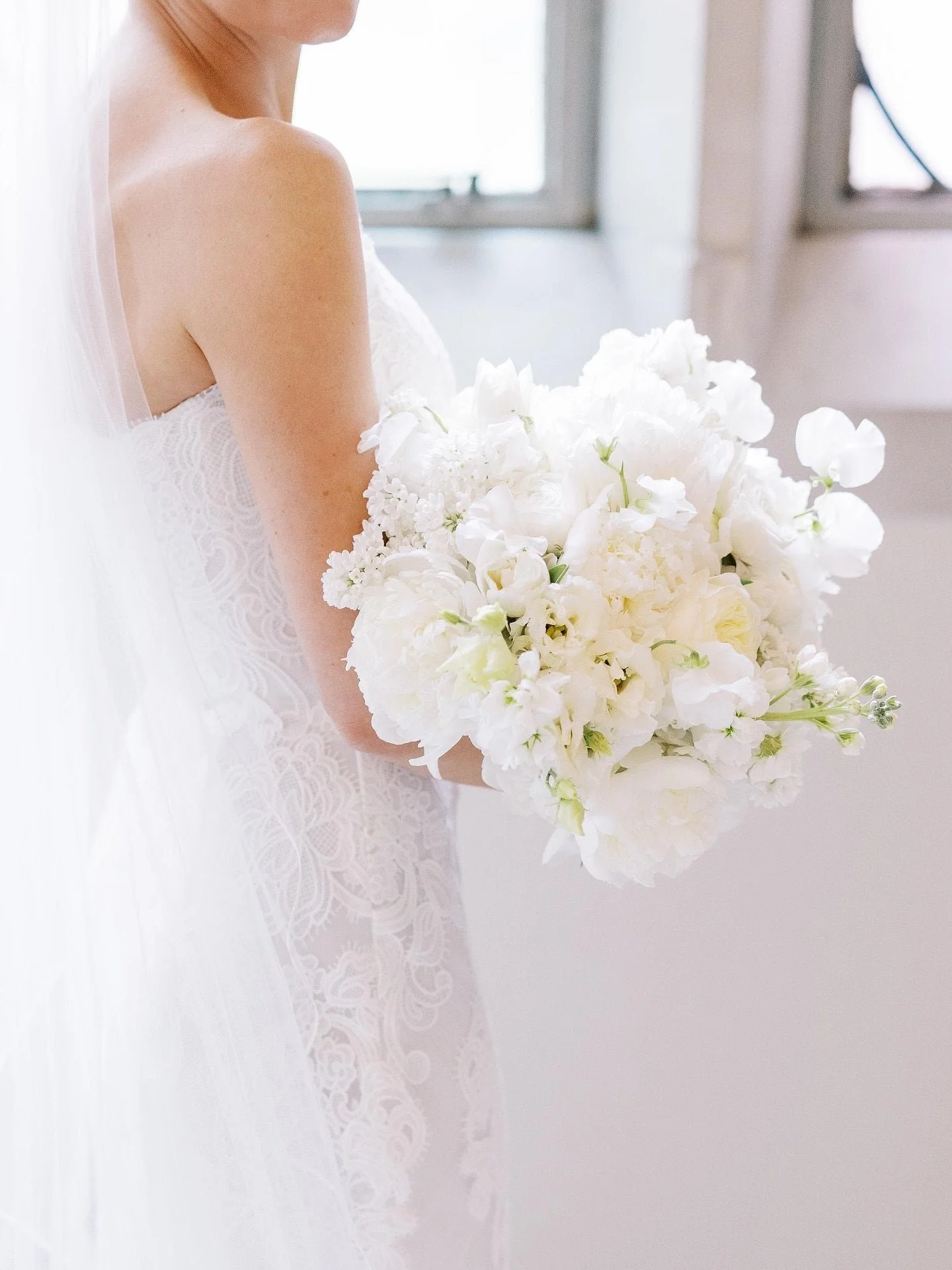A bride wearing a lace wedding dress holding a large bouquet of white flowers.