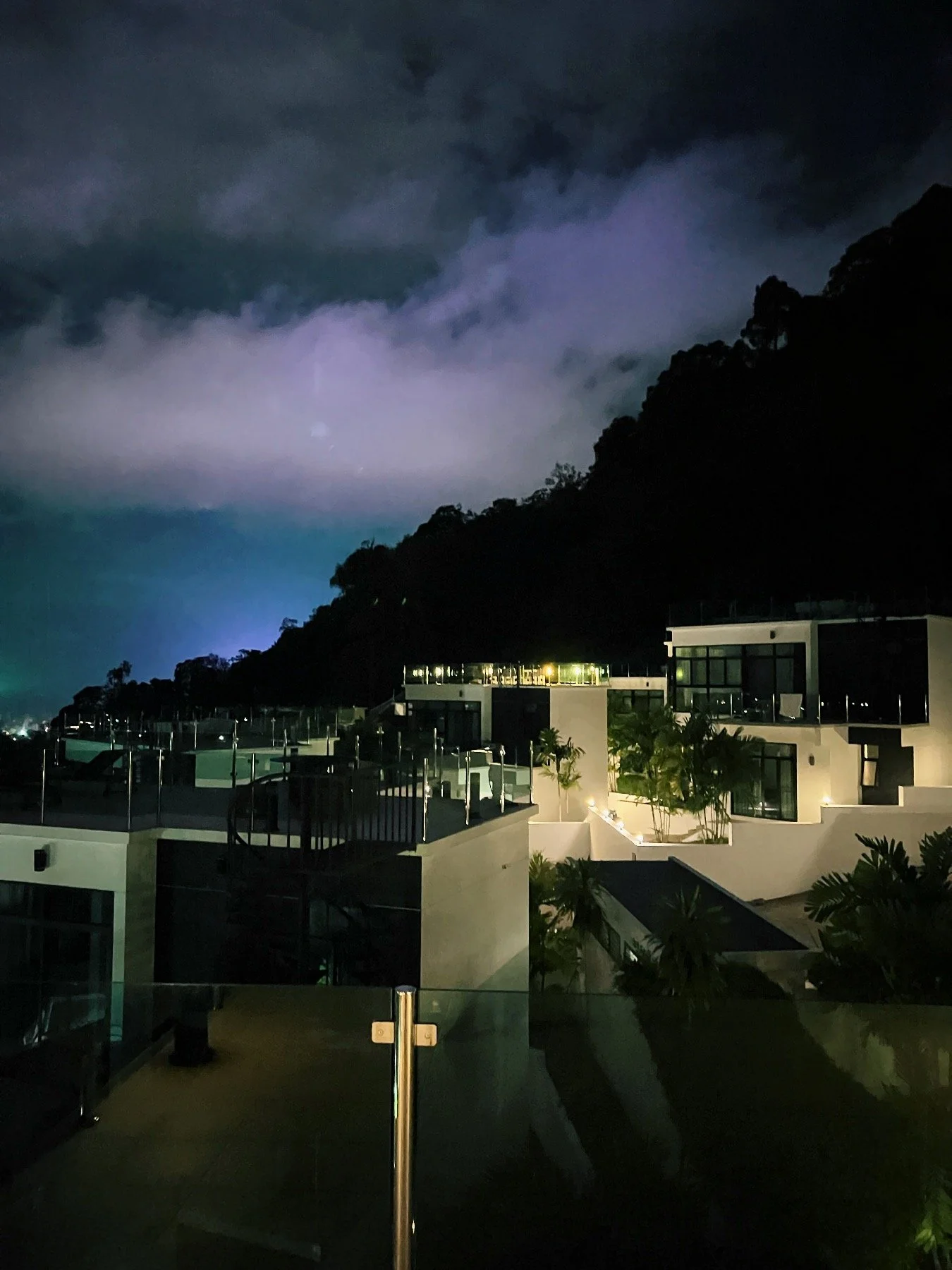 Night view of modern houses on a hillside with clouds and mountains in the background.