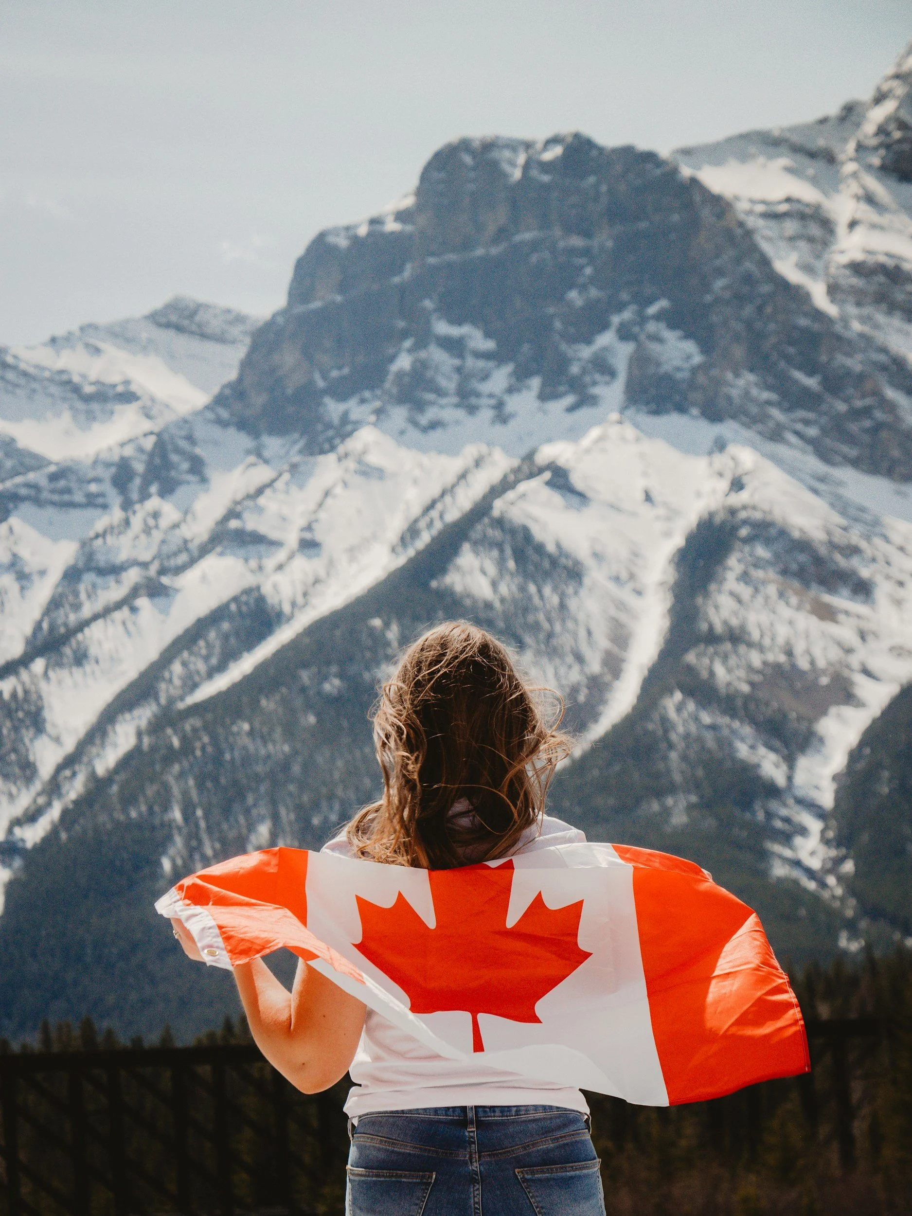 Person holding a Canadian flag in front of snowy mountains.