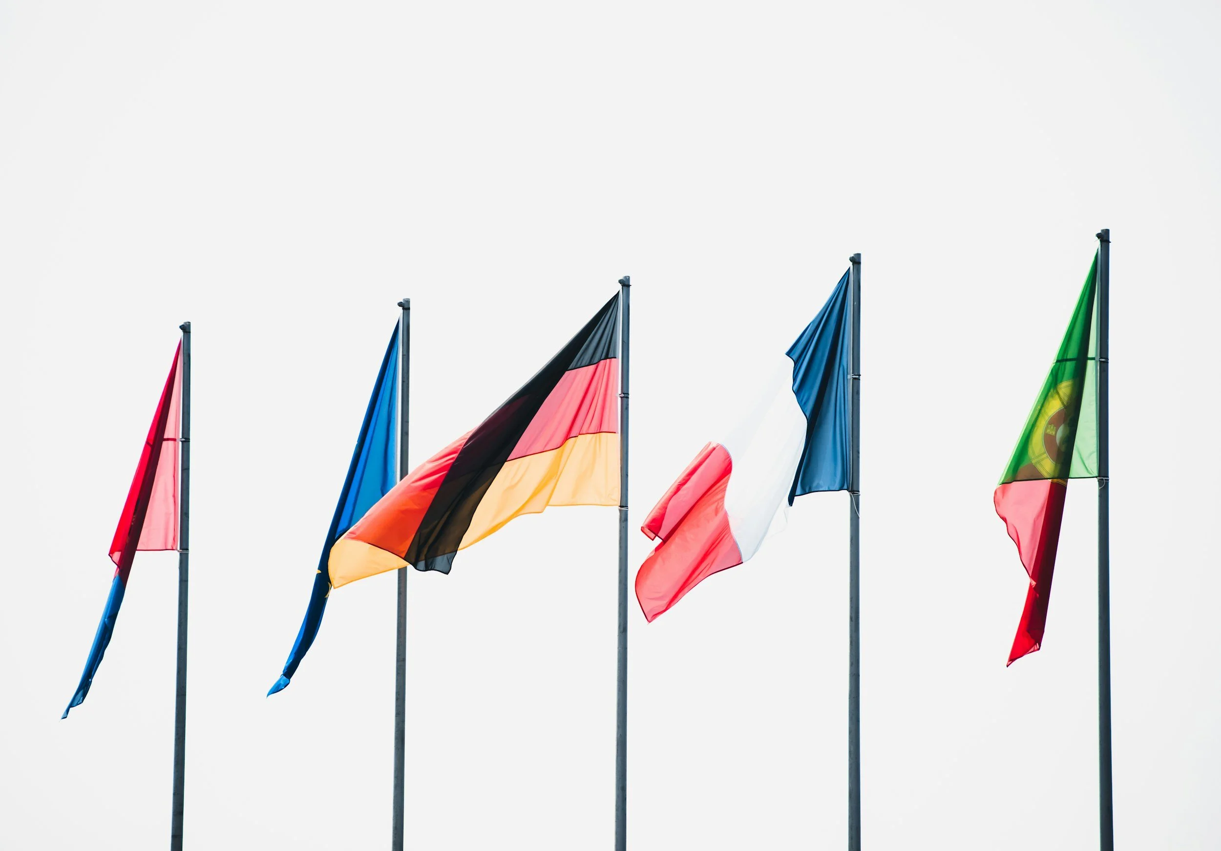 Five flags on poles against a clear sky, including German, French, and Portuguese flags.