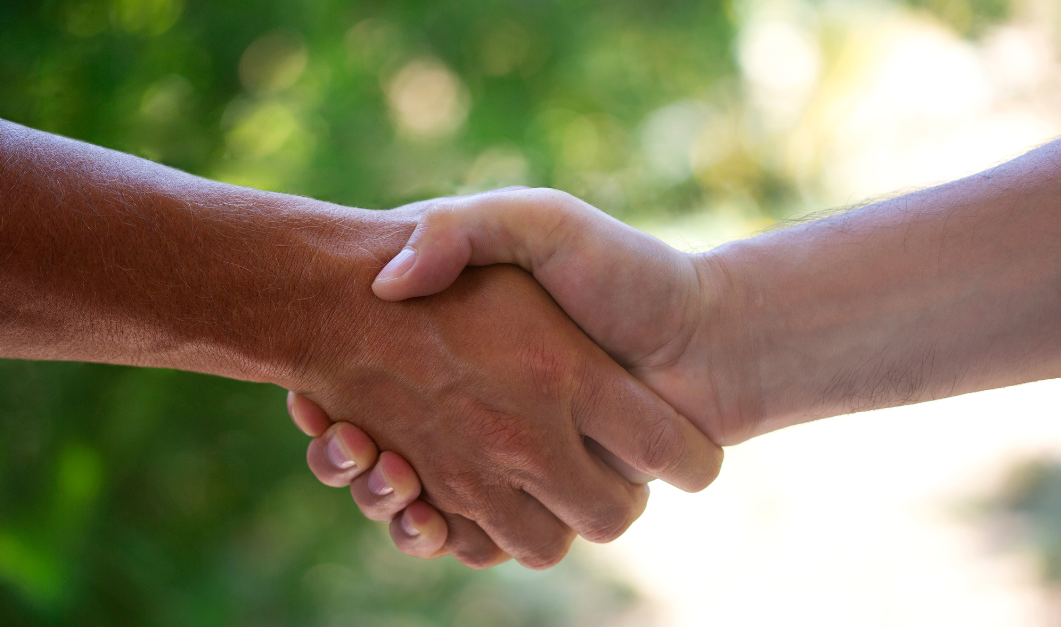 Two people shaking hands outdoors with a blurred green natural background.