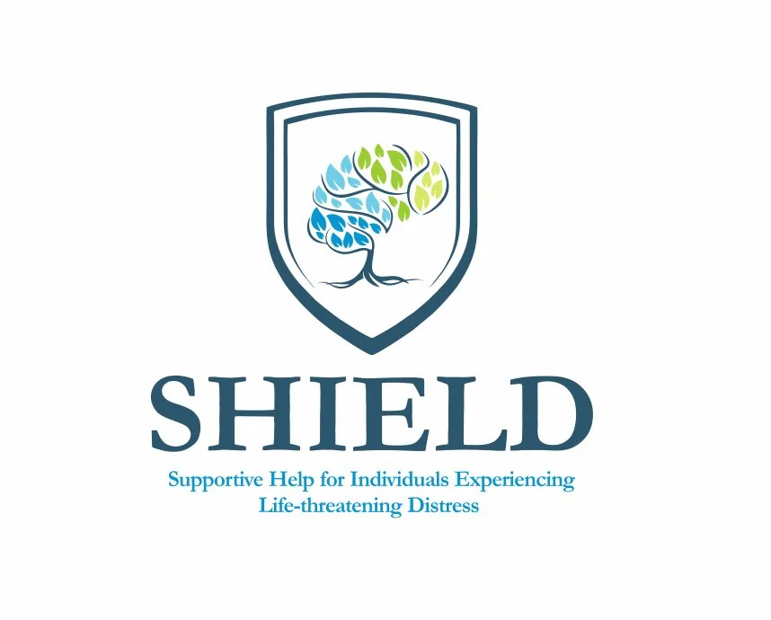 Logo of SHIELD with a shield emblem containing a stylized tree with blue and green leaves and roots, and the text "SHIELD" below it, with the slogan "Supportive Help for Individuals Experiencing Life-threatening Distress."