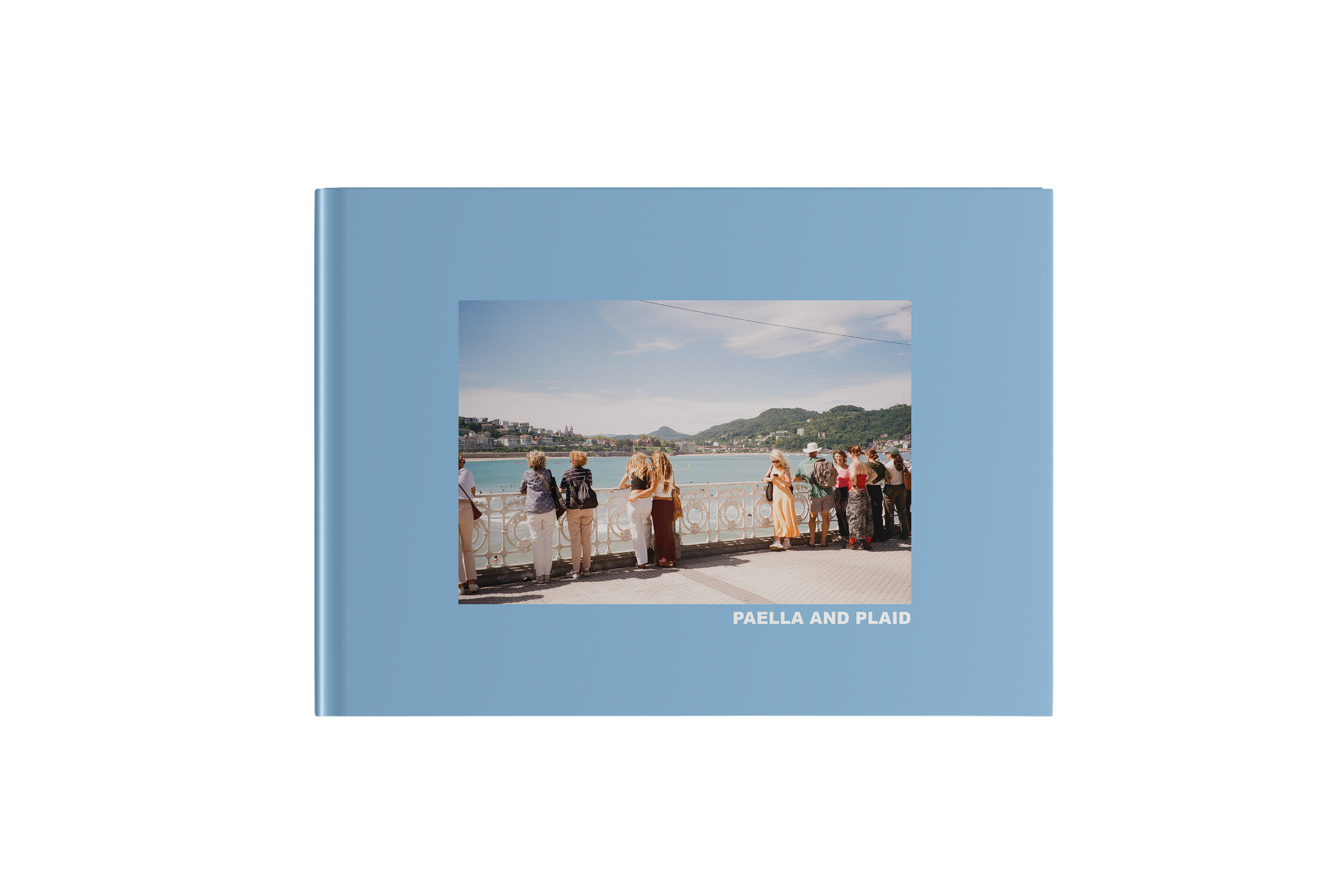 A group of people standing by a railing overlooking a body of water and hills, on the cover of a blue book titled "Paella and Plaid."