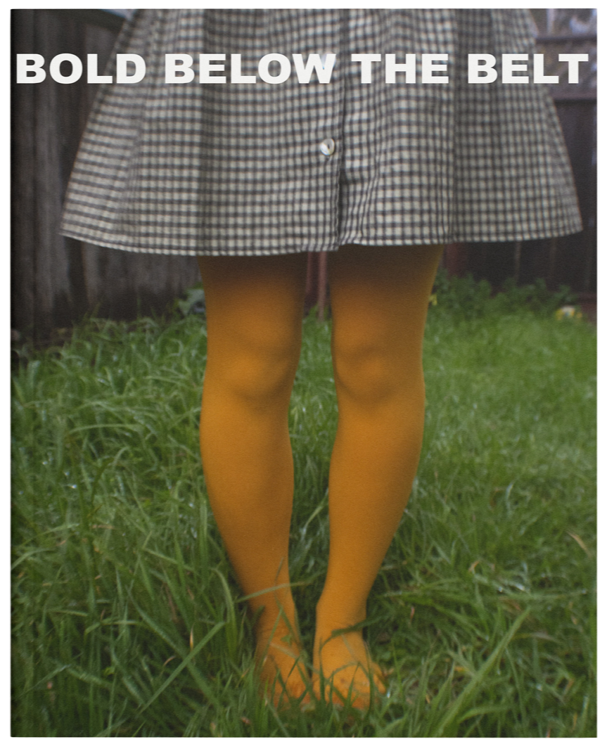 Person wearing yellow tights and a checkered skirt standing in grass with a wooden fence in the background, with text overlay saying 'BOLD BELOW THE BELT'.