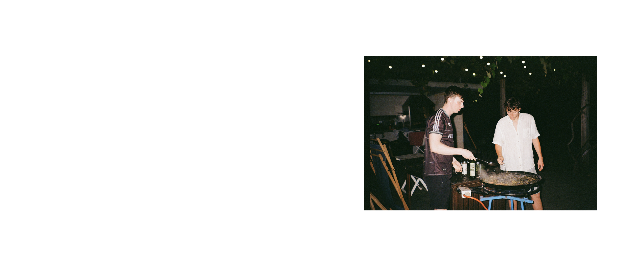 Two young men cooking outdoors at night, one stirring a large pan, the other watching, surrounded by string lights and outdoor furniture.