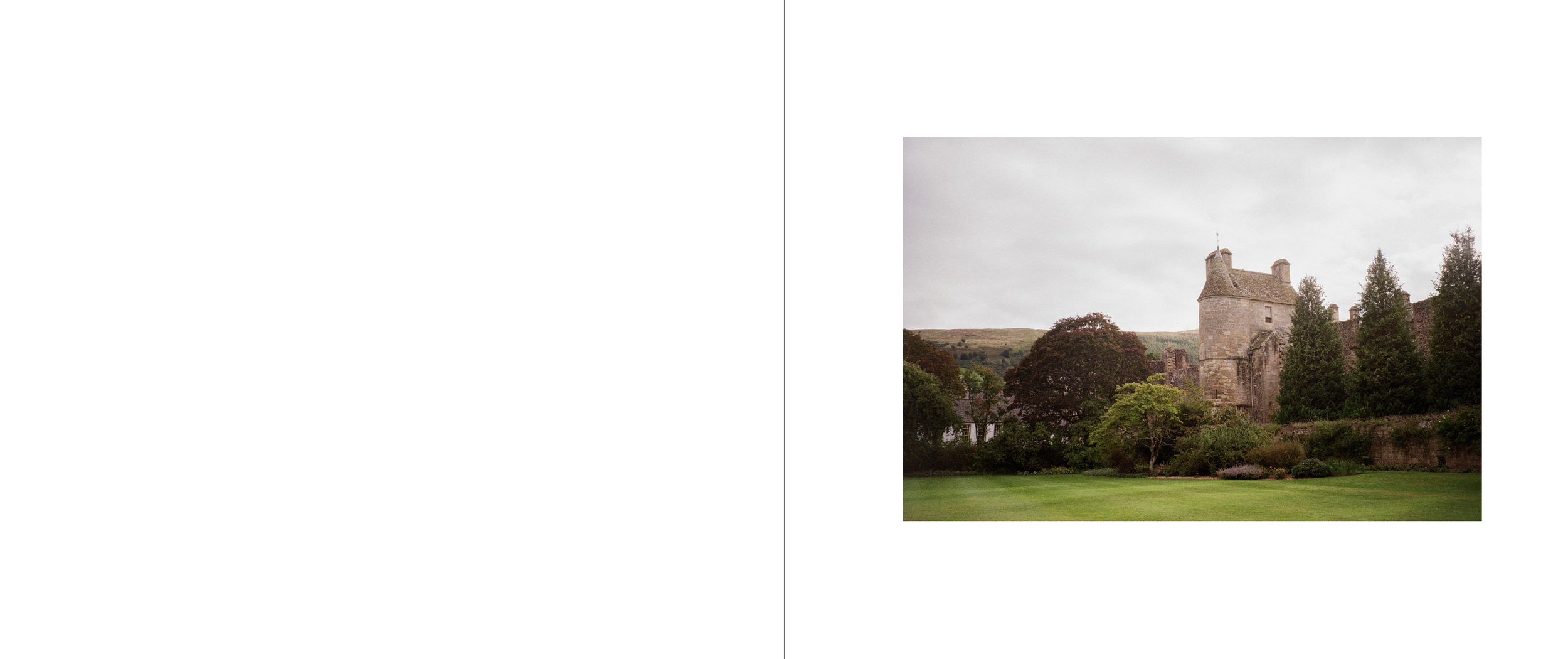 A historic stone castle with turrets, surrounded by green trees and a manicured lawn, under an overcast sky.