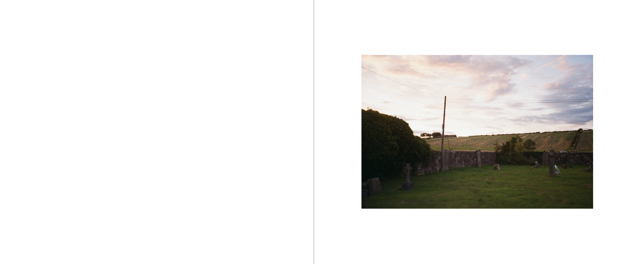 Sunset over a rural cemetery with headstones, a stone wall, a utility pole, and rolling green hills in the background.
