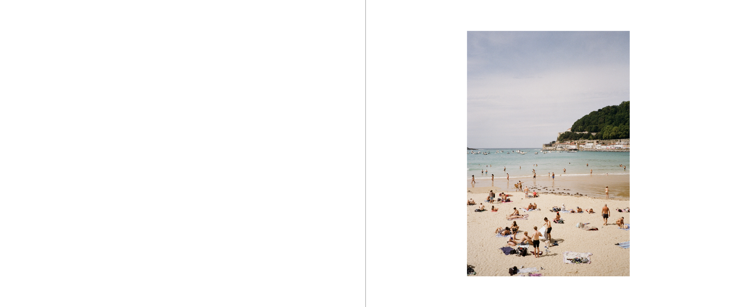 People relaxing and swimming on a sandy beach with a hill and buildings in the background, under a partly cloudy sky.