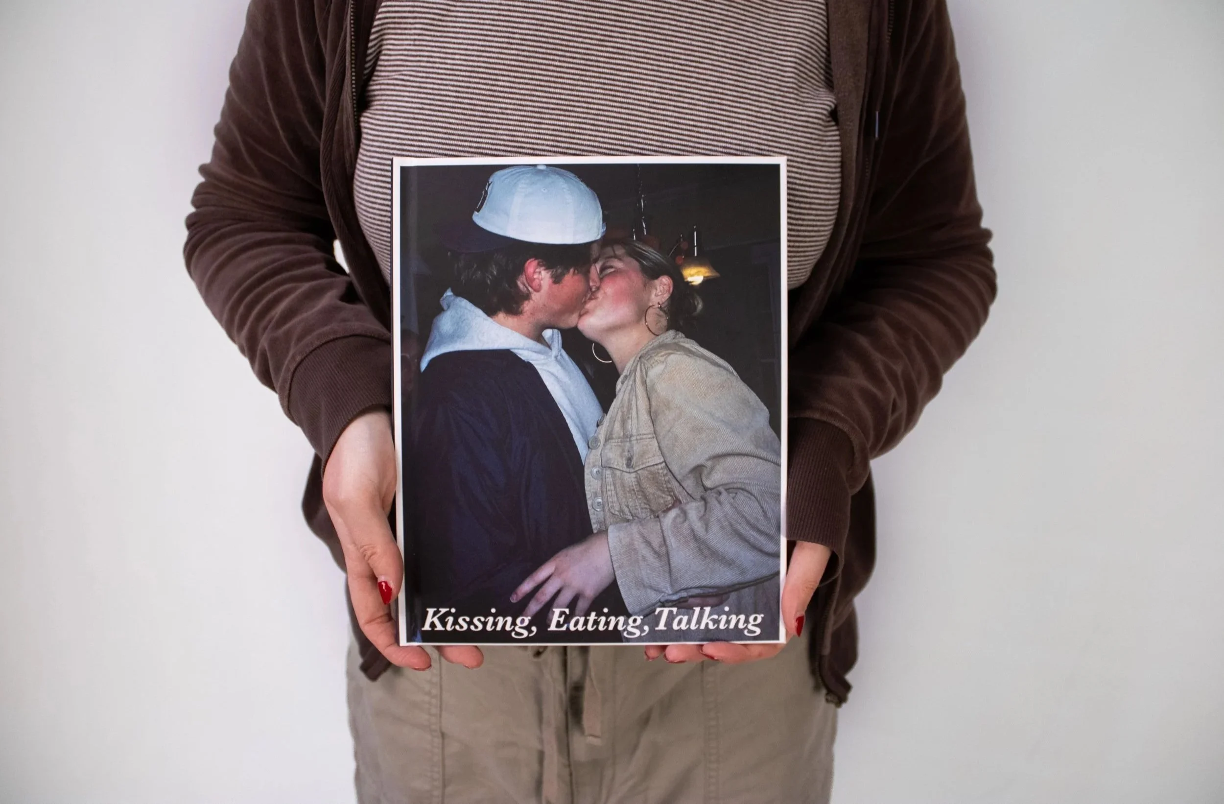 Person holding a book with a cover photo of kissing couple, and the text 'Kissing, Eating, Talking'.