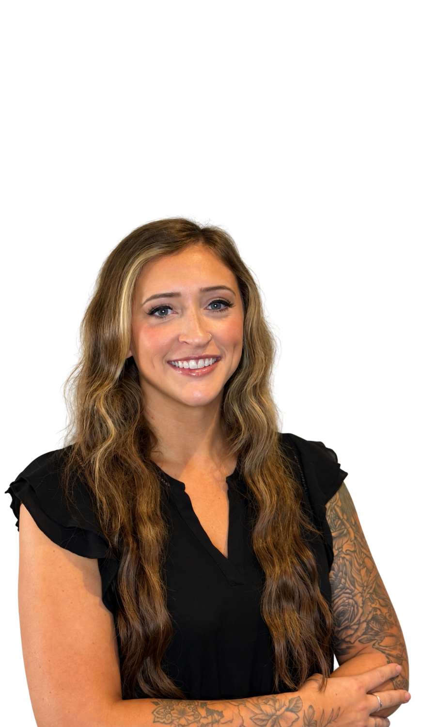 Portrait of a smiling woman with long wavy hair, wearing a black top, and showing tattoos on her arms.