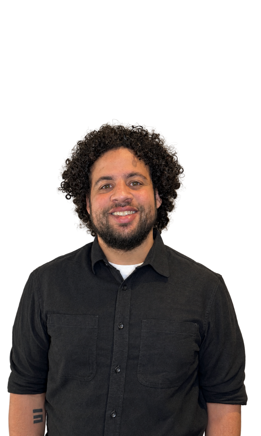 A man with curly hair and a beard smiling, wearing a black button-up shirt with rolled-up sleeves, standing against a plain background.