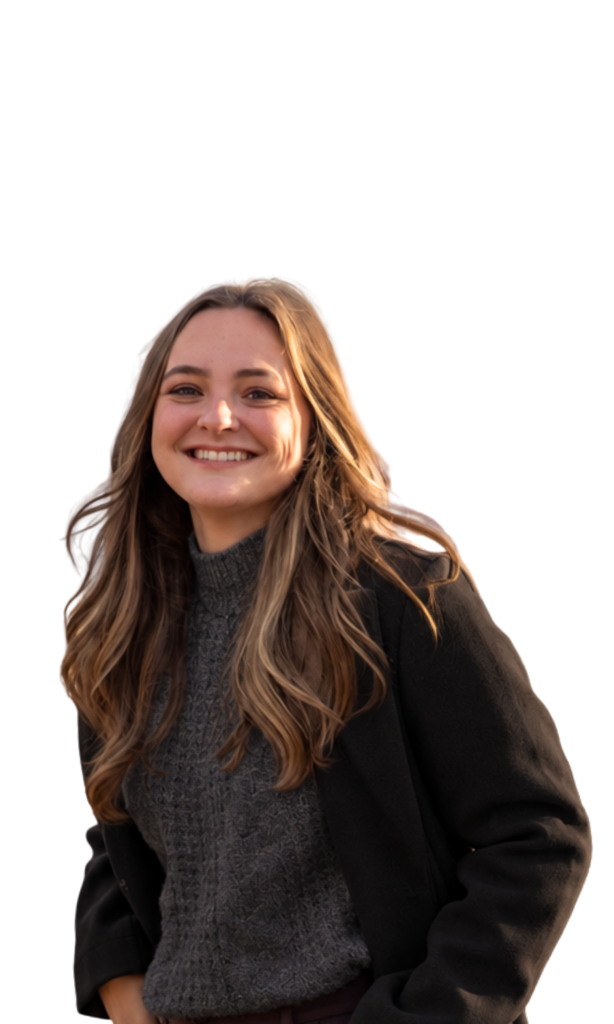 A young woman with long wavy light brown hair, smiling, wearing a dark coat and a gray sweater.