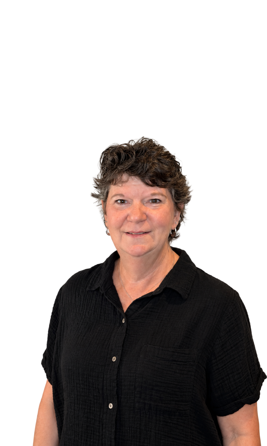 A middle-aged woman with short, curly, brown hair and light skin, wearing a black button-up shirt, smiling gently, against a black background.