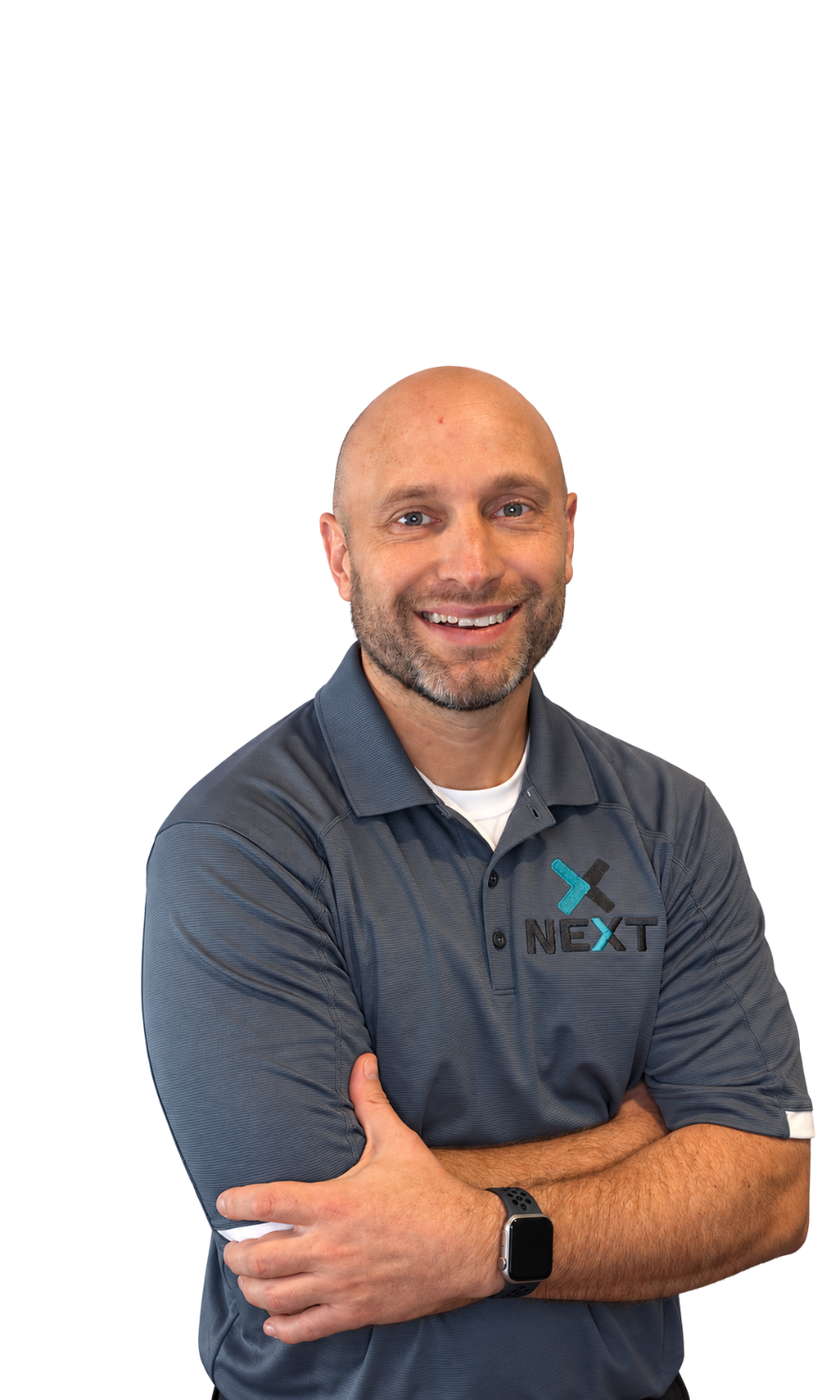 A man with a beard and shaved head smiling with arms crossed, wearing a dark gray polo shirt with a logo that says 'NEXT' and a smartwatch on his left wrist.