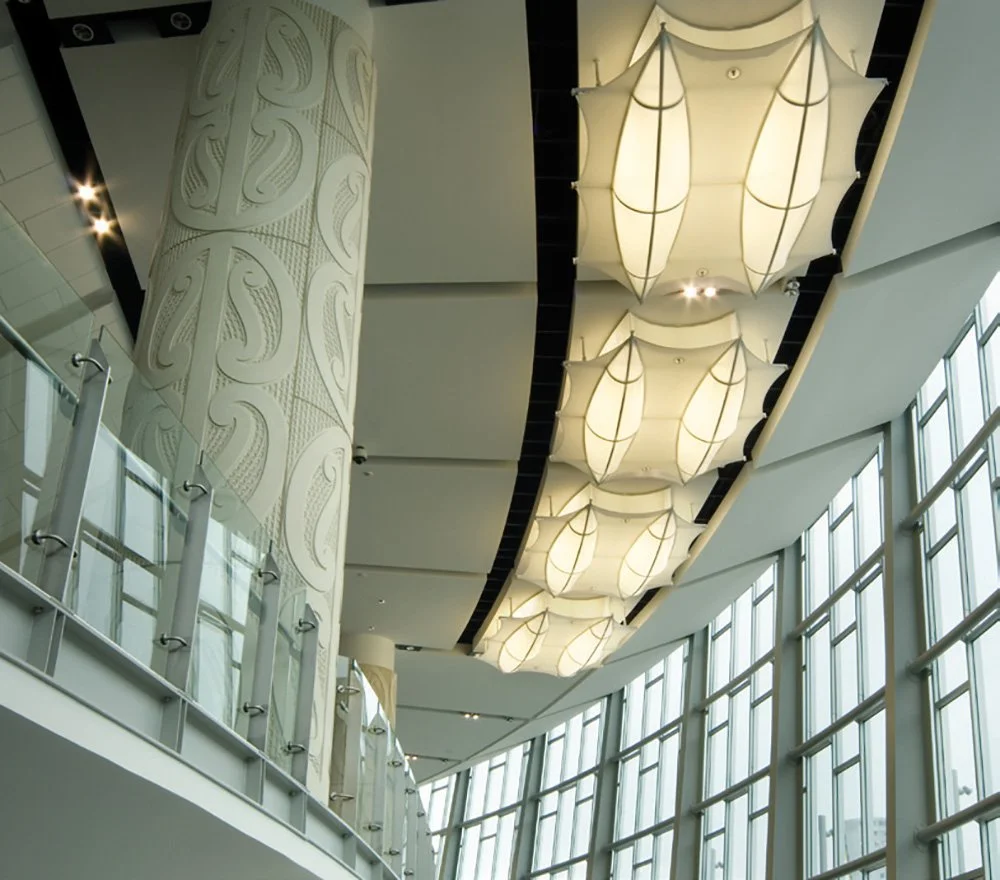 Interior of a modern building with large windows, ornate hanging ceiling lights, and decorative columns.