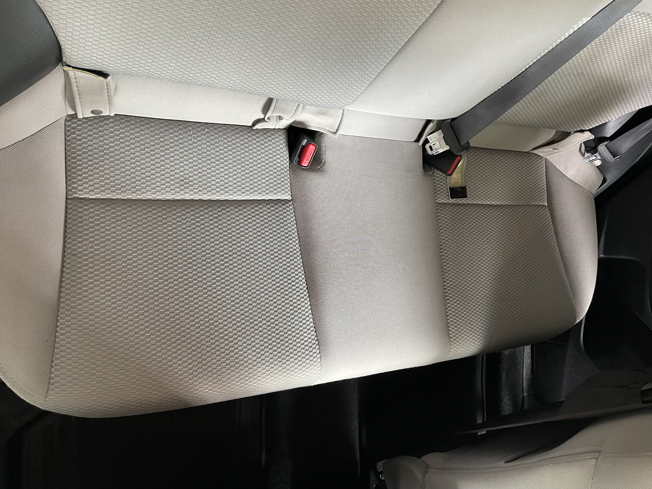 Car interior, beige rear seat with textured fabric and seat belts.