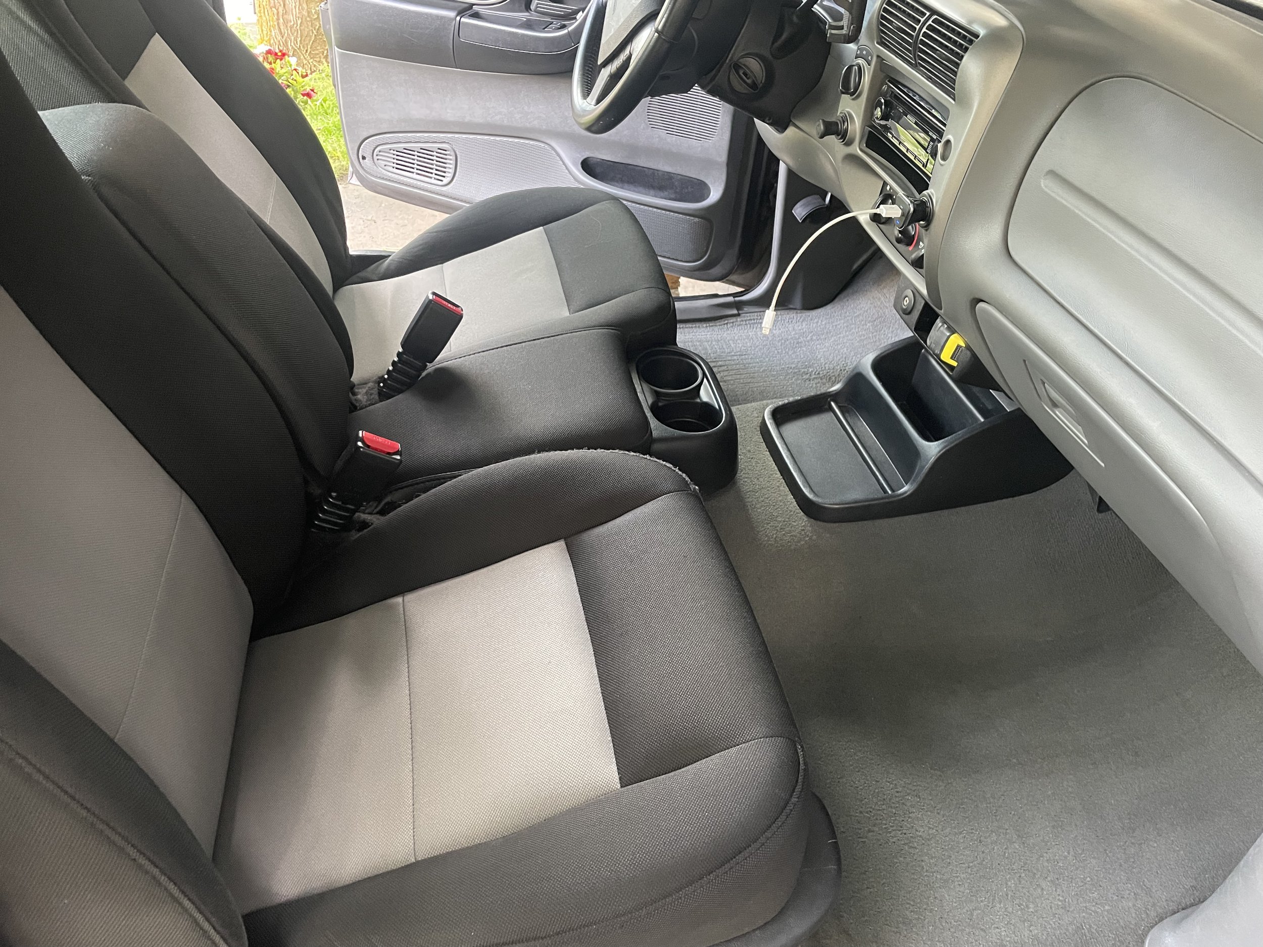 Car interior with black and gray seats, open front door, dashboard, steering wheel, and cup holders; minimalistic design.