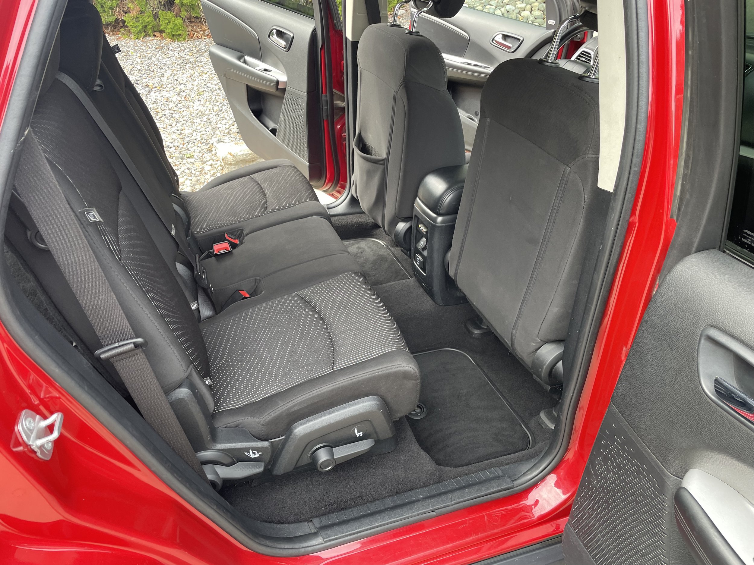 Interior of a red car showing the backseat area with black fabric seats and open doors.