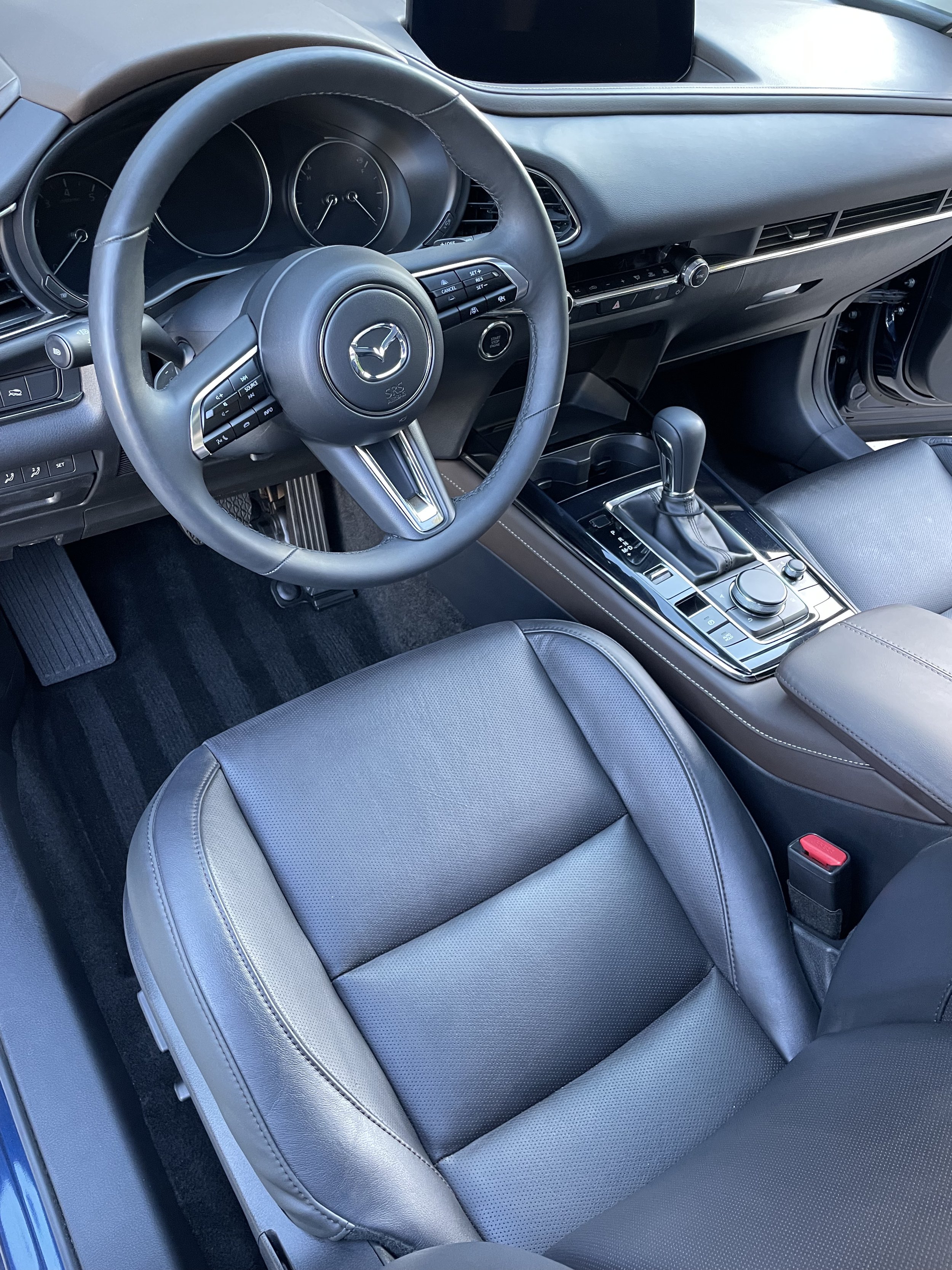 Interior of a Mazda car showing steering wheel, dashboard, gear shift, and leather seat.