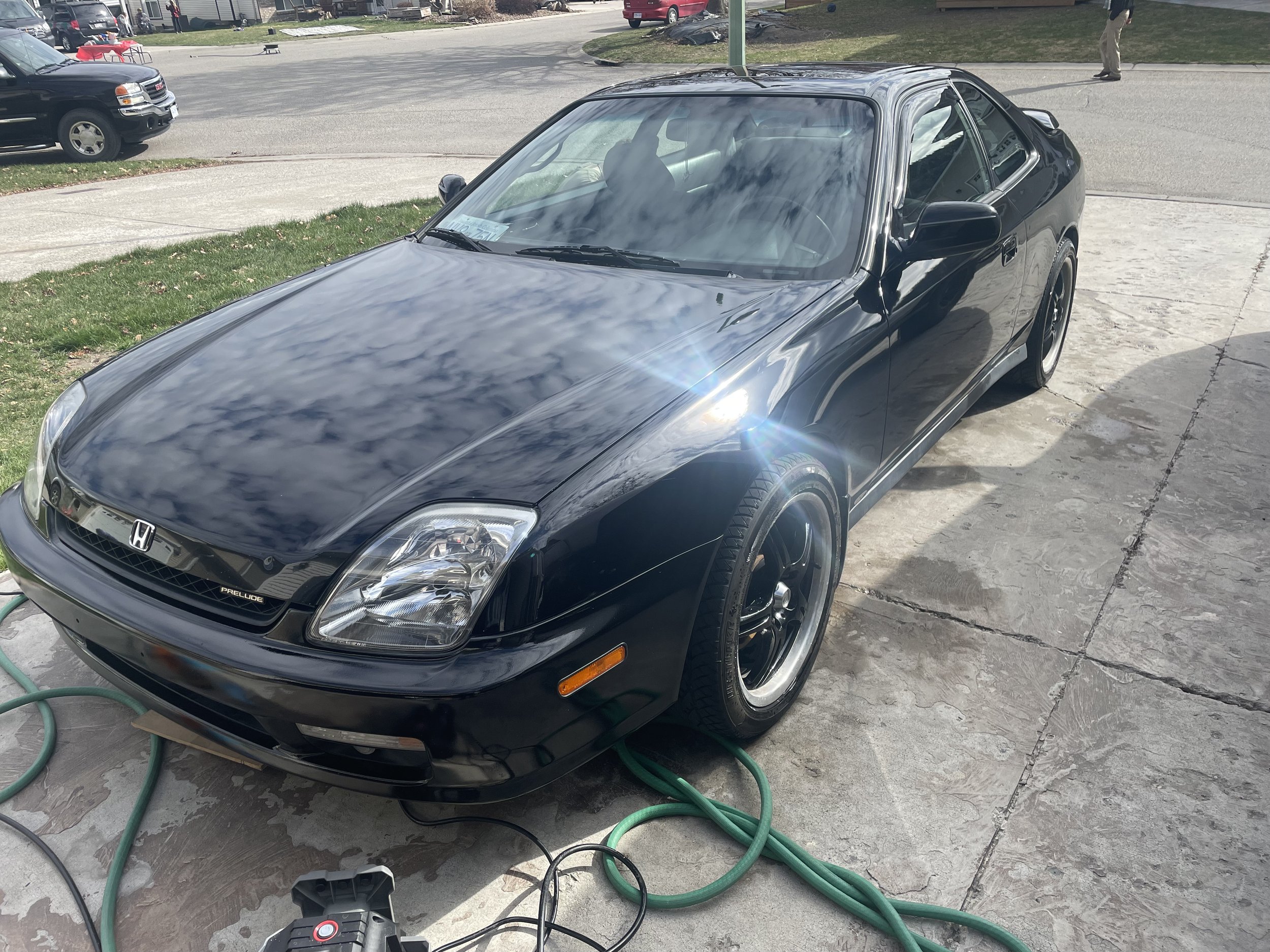 Black Honda Prelude car parked on a driveway with hoses and cleaning equipment around it.