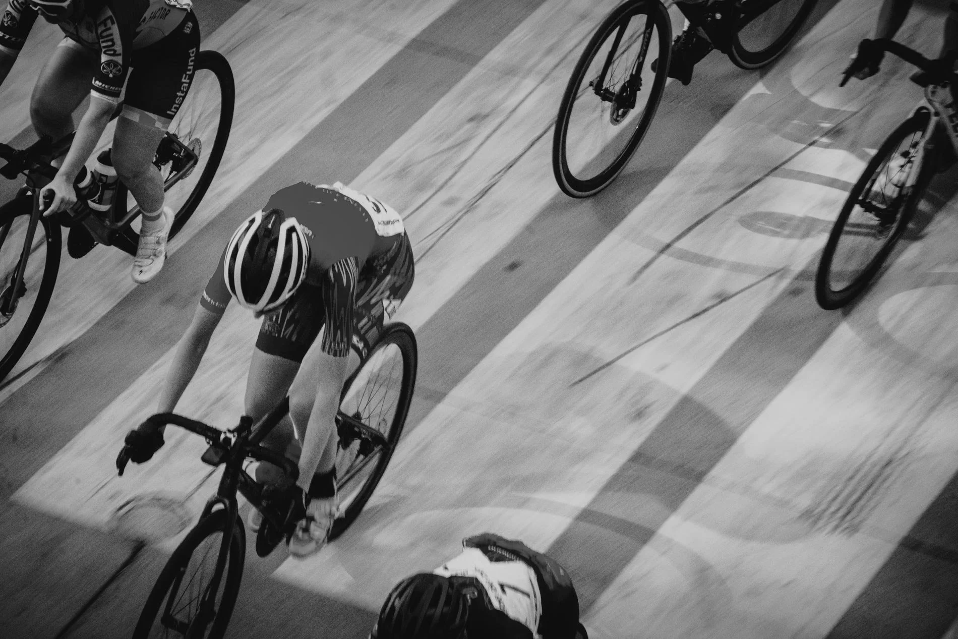Cyclists racing on an indoor track, viewed from above, in black and white.