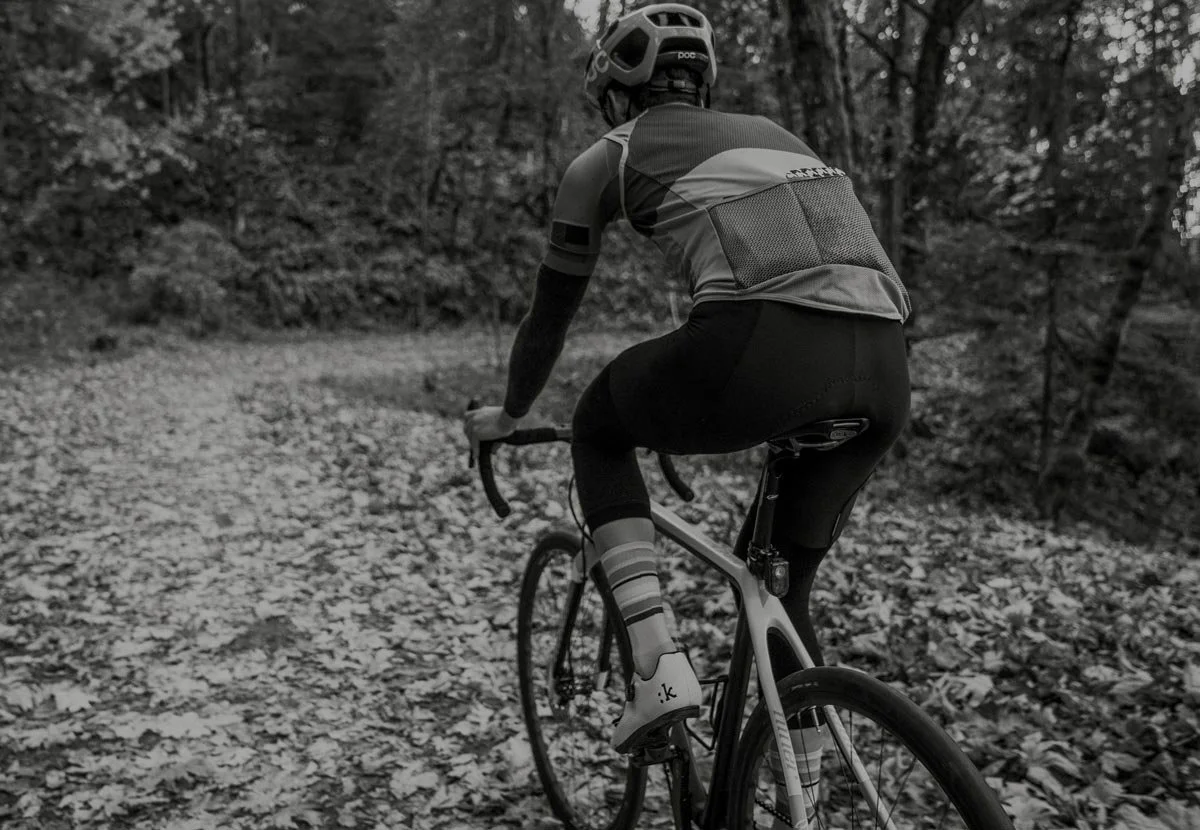 A person cycling on a trail through a wooded area, wearing a helmet, sports clothing, and striped socks.