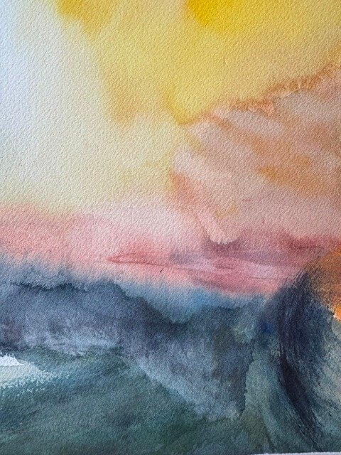 Close-up of soft golden and pink watercolor clouds blending above a shadowed sea.