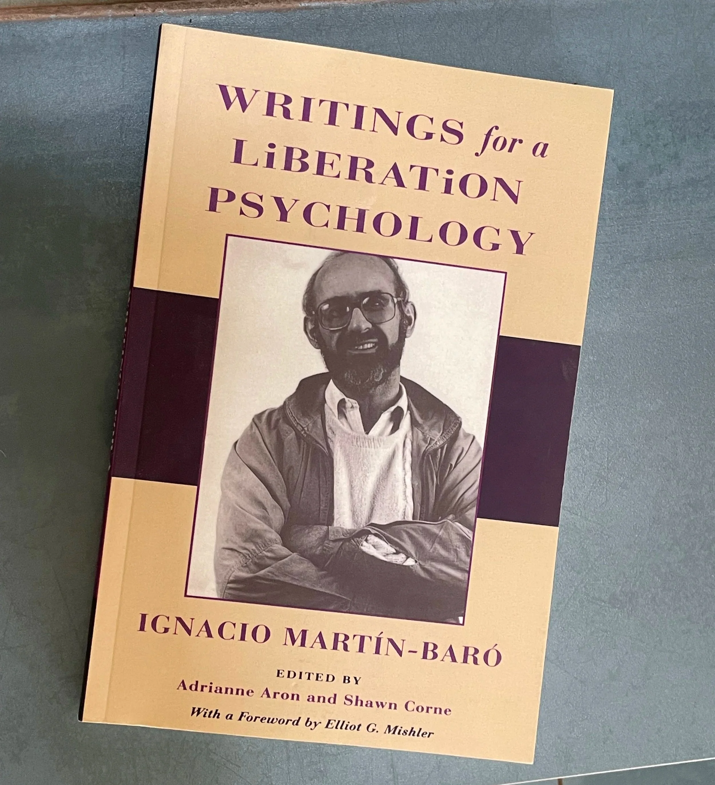 Book titled 'Writings for a Liberation Psychology' by Ignacio Martín-Baró, with a photo of the author on the cover, lying on a blue-grey surface.