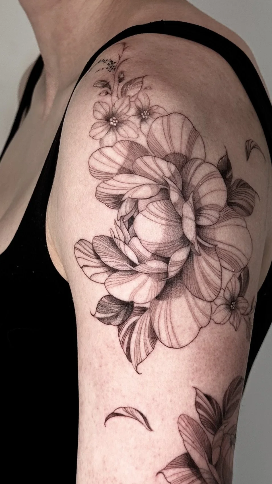 Black and gray floral tattoo on a person's arm, featuring detailed blossoms, leaves, and petals.