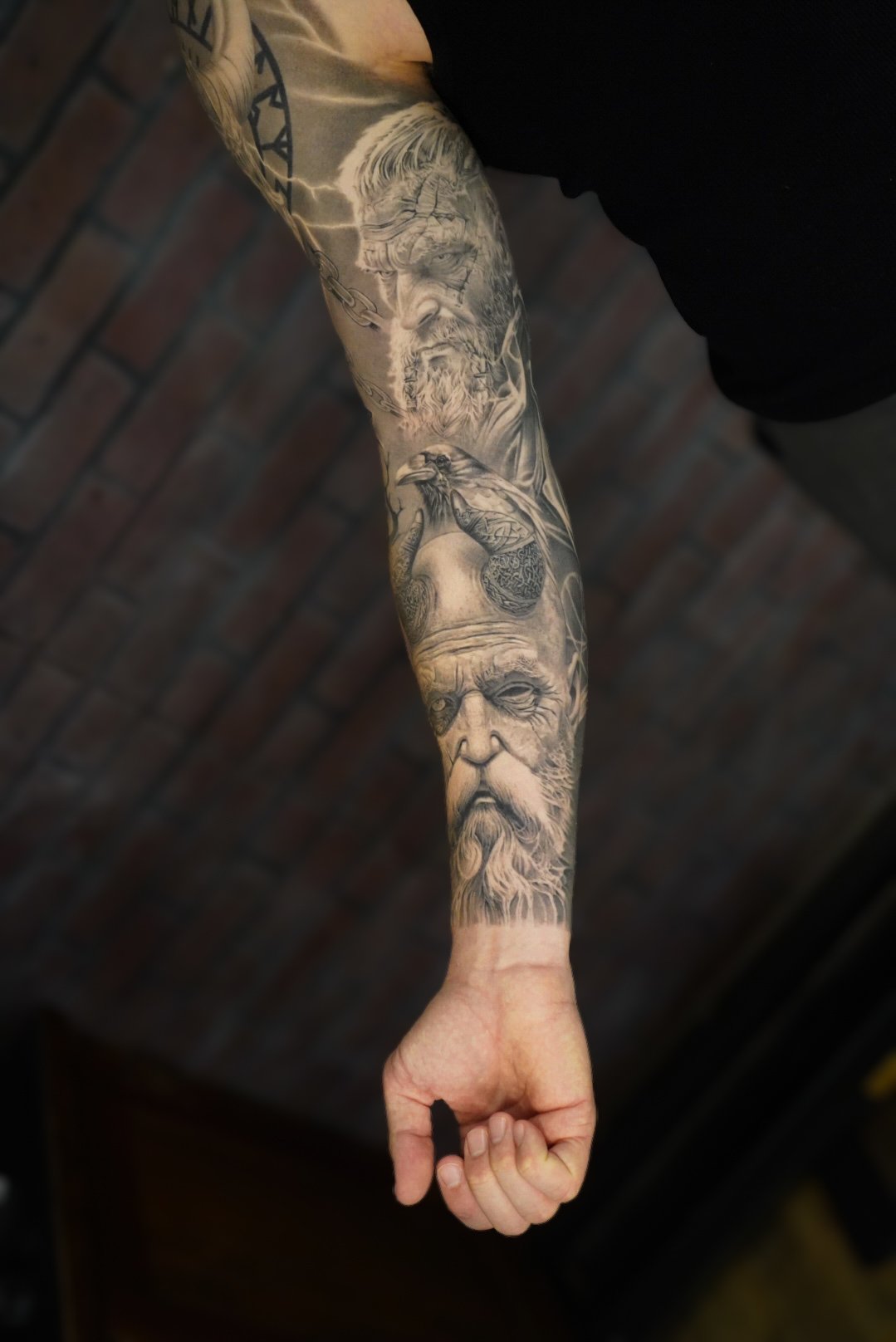 Tattoo sleeve on person's arm featuring detailed grayscale portraits of three elderly men's faces with beards and a crow perched on a branch.