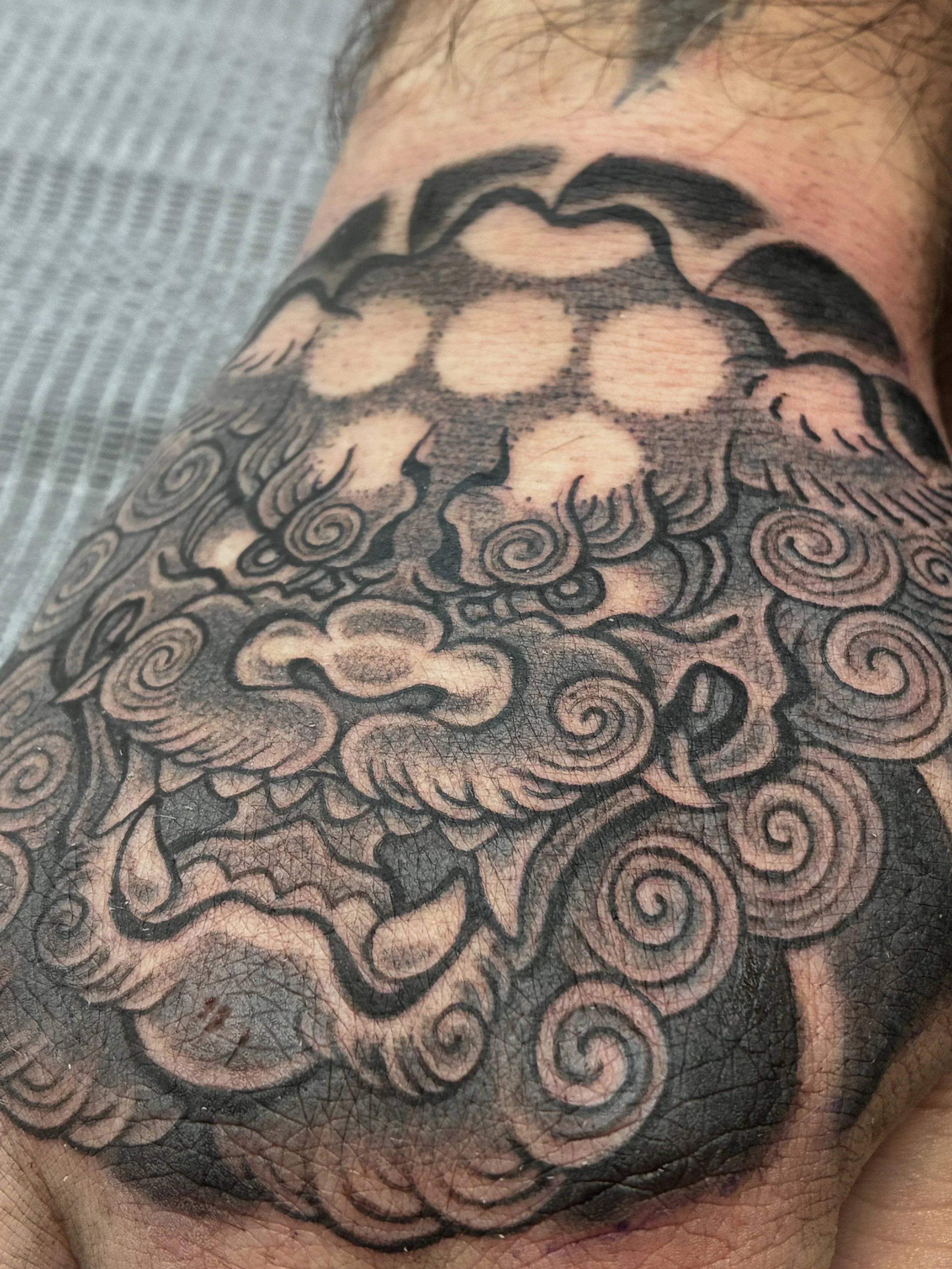Close-up of a person's skin with an intricate black tattoo featuring swirling lines and patterns.