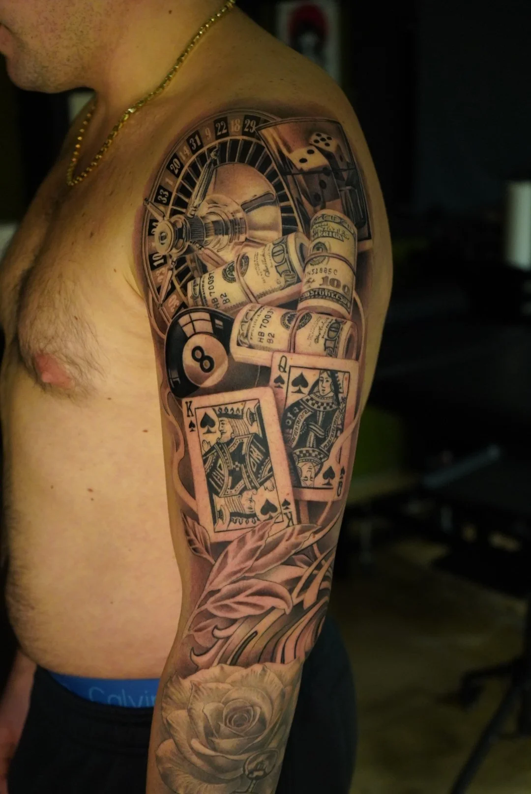 Tattoo of casino elements including dice, rolled bills, poker chips, and playing cards on a person's upper arm and shoulder.