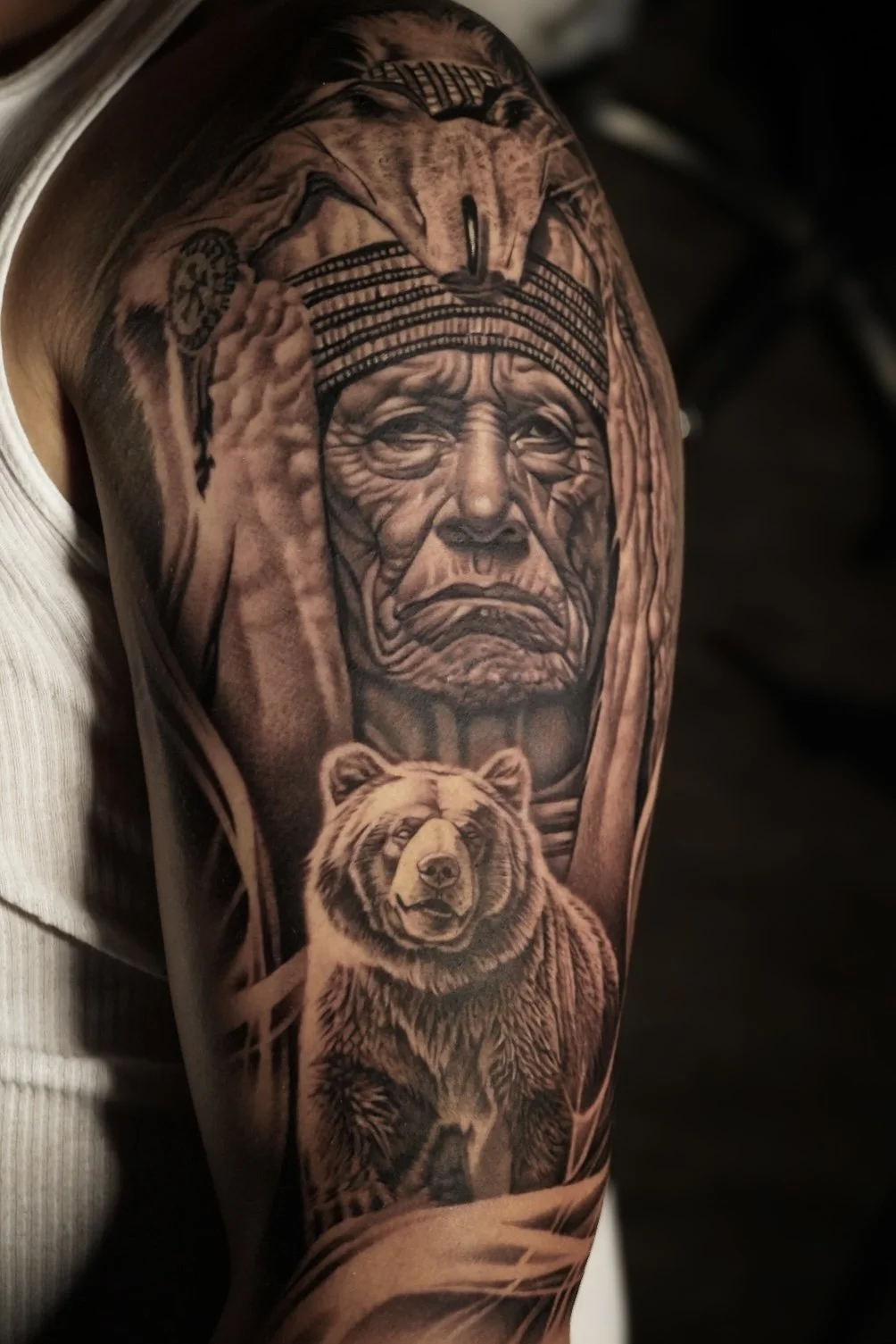 Tattoo of a Native American elder and a bear on an upper arm.
