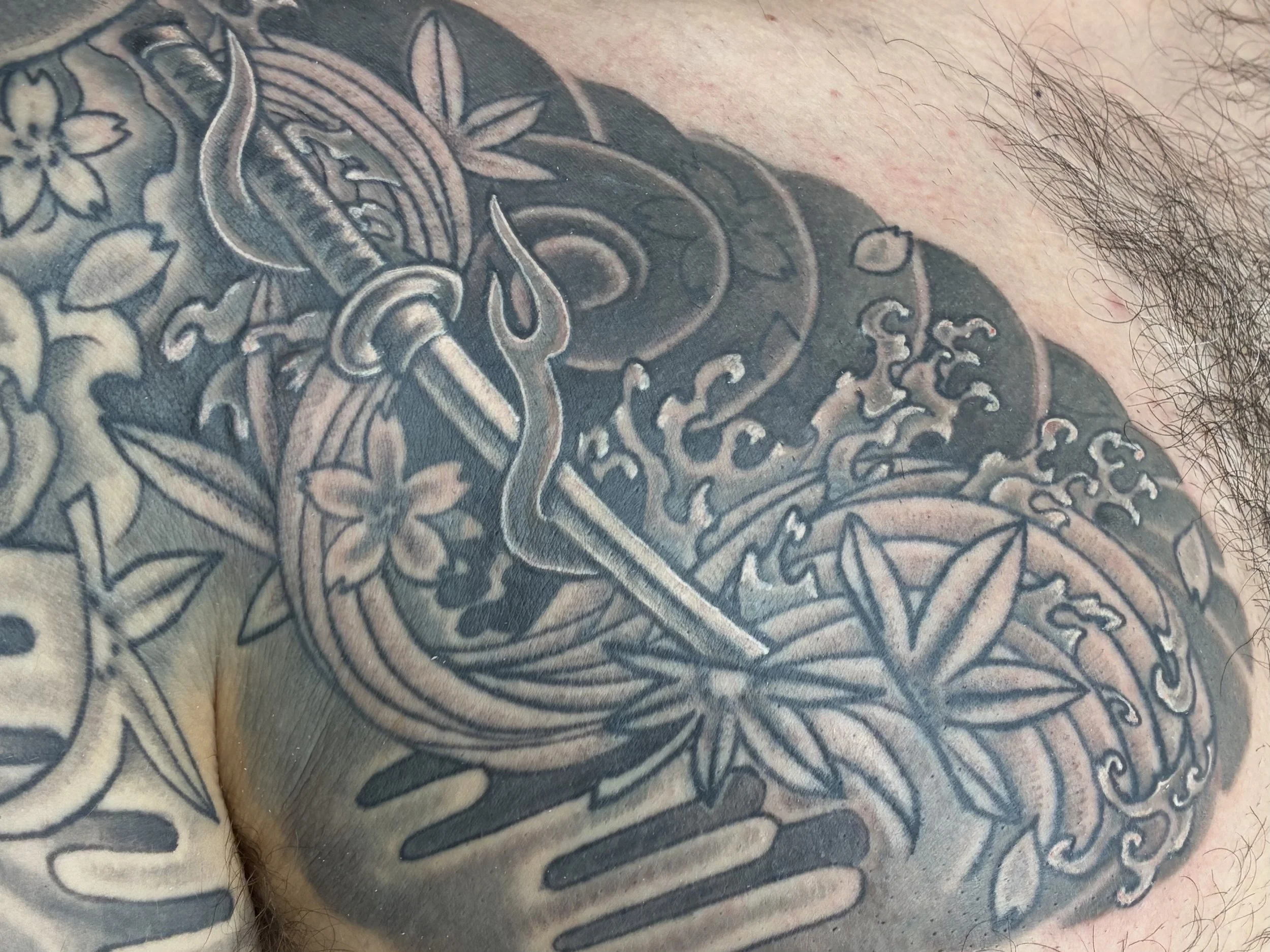 Close-up of a person's chest tattoo with floral and abstract designs, including a prominent flower and swirling patterns.