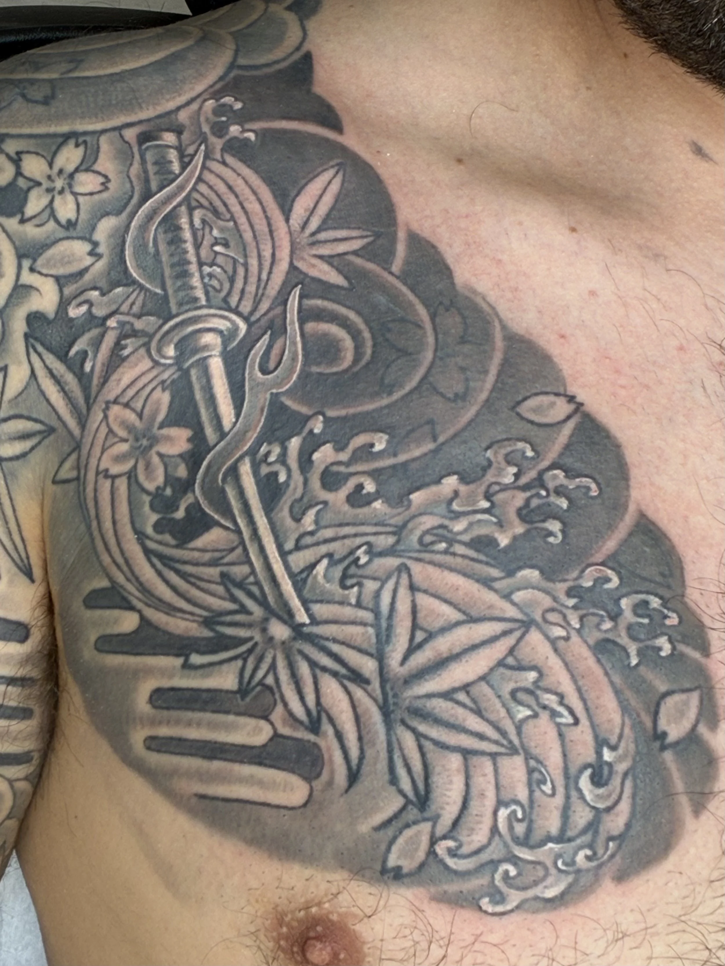 Close-up of a person's chest with detailed black and gray tattoo featuring flowers, a sword, and a snake.