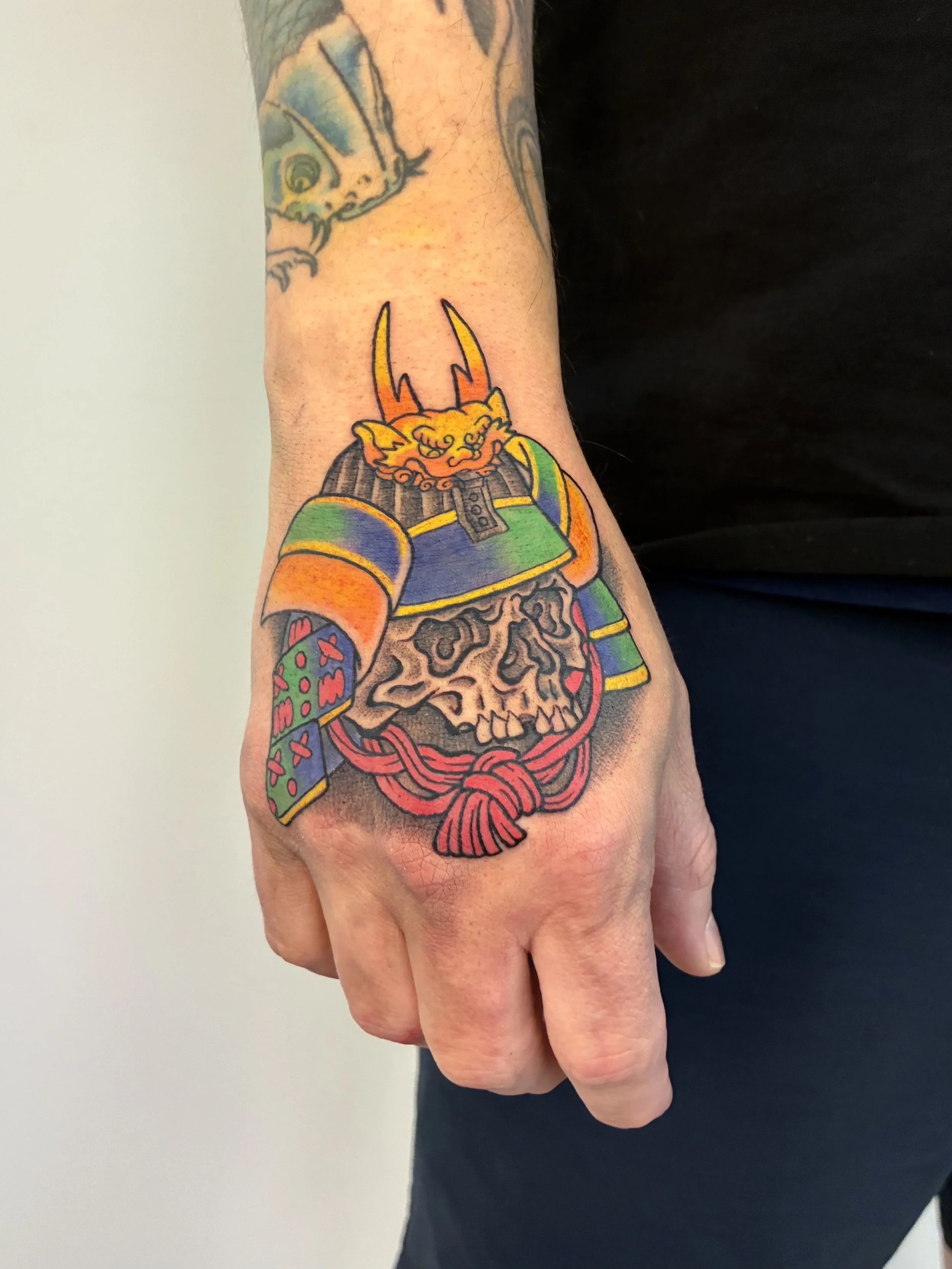Tattoo of a colorful Oni mask on a person's forearm, with an artistic skull tattoo nearby.