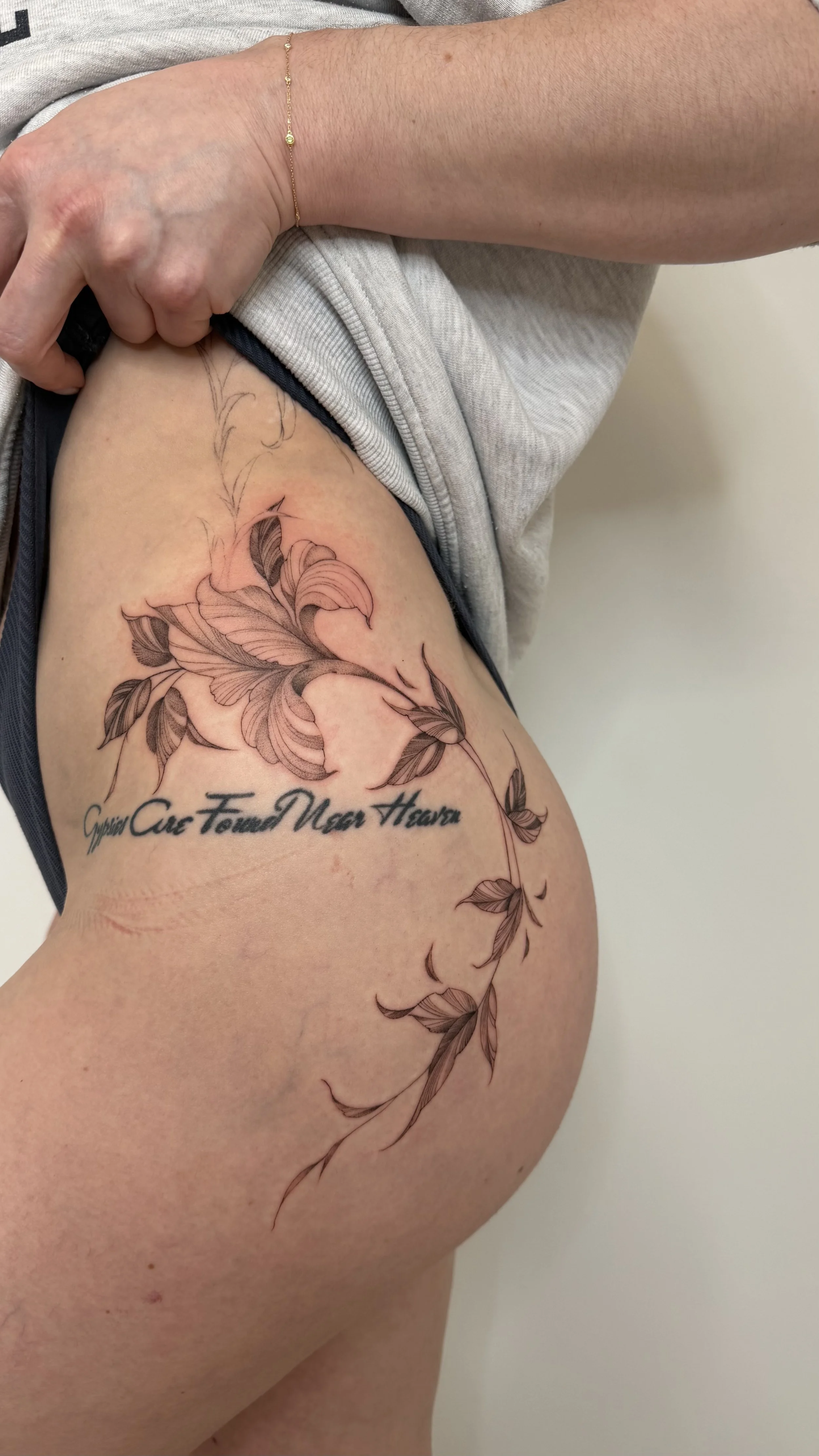 A tattoo of a floral design with leaves and a stem on the person's thigh, along with the quote 'Cypress Cause Found Near Heart.'