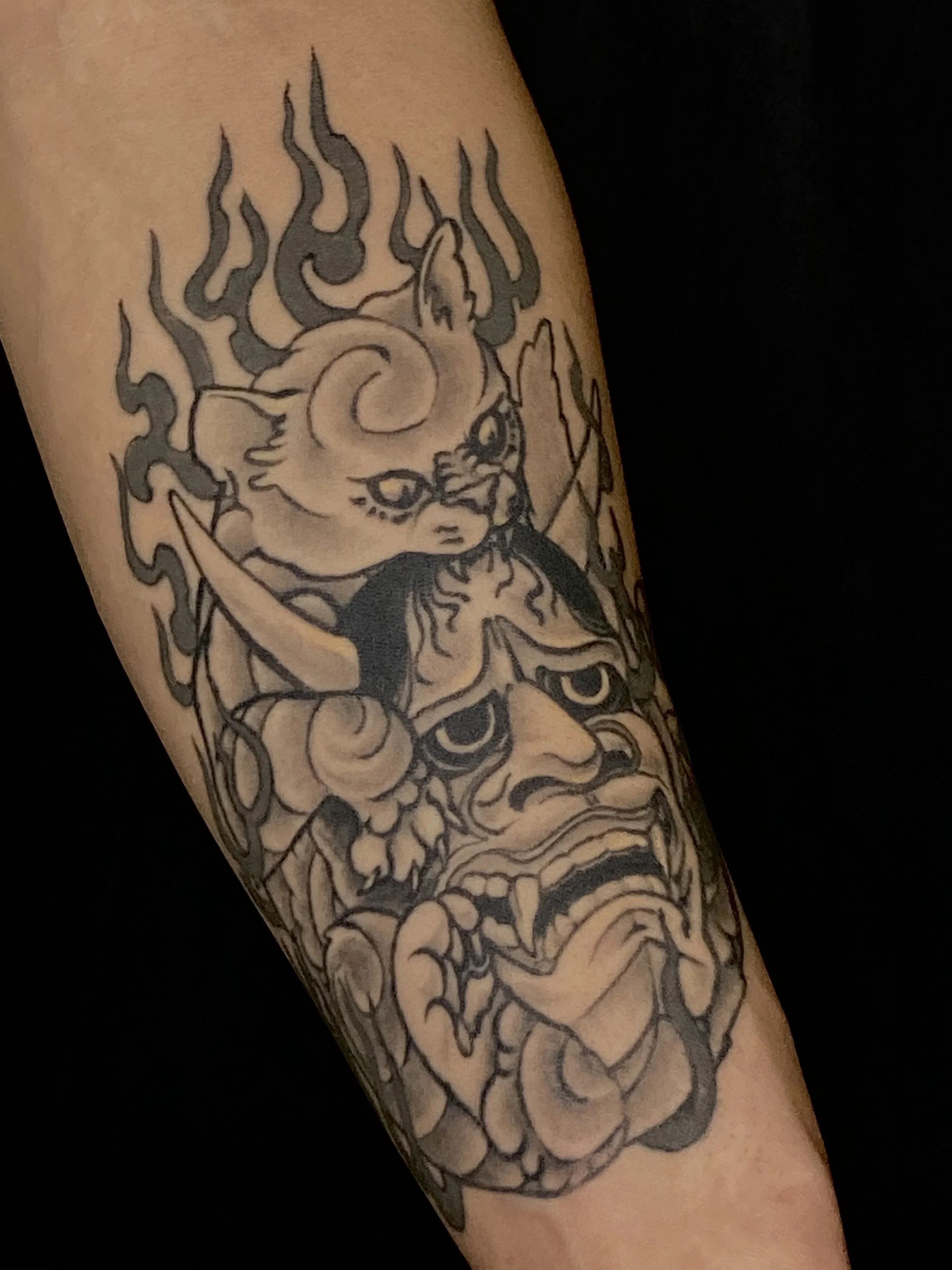 Black and gray tattoo of a skull with swirling flames on arm.