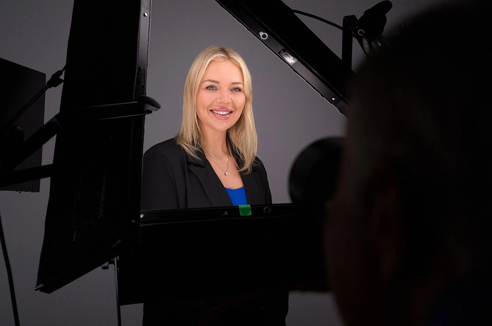 Professional woman with blonde hair smiling at camera during a photo shoot, seen through the frame of a camera or lighting equipment.