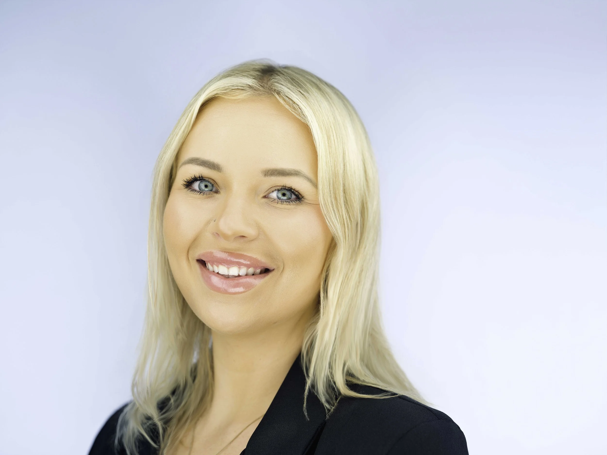 Professional headshot of a blonde woman in a black jacket against a clean light background