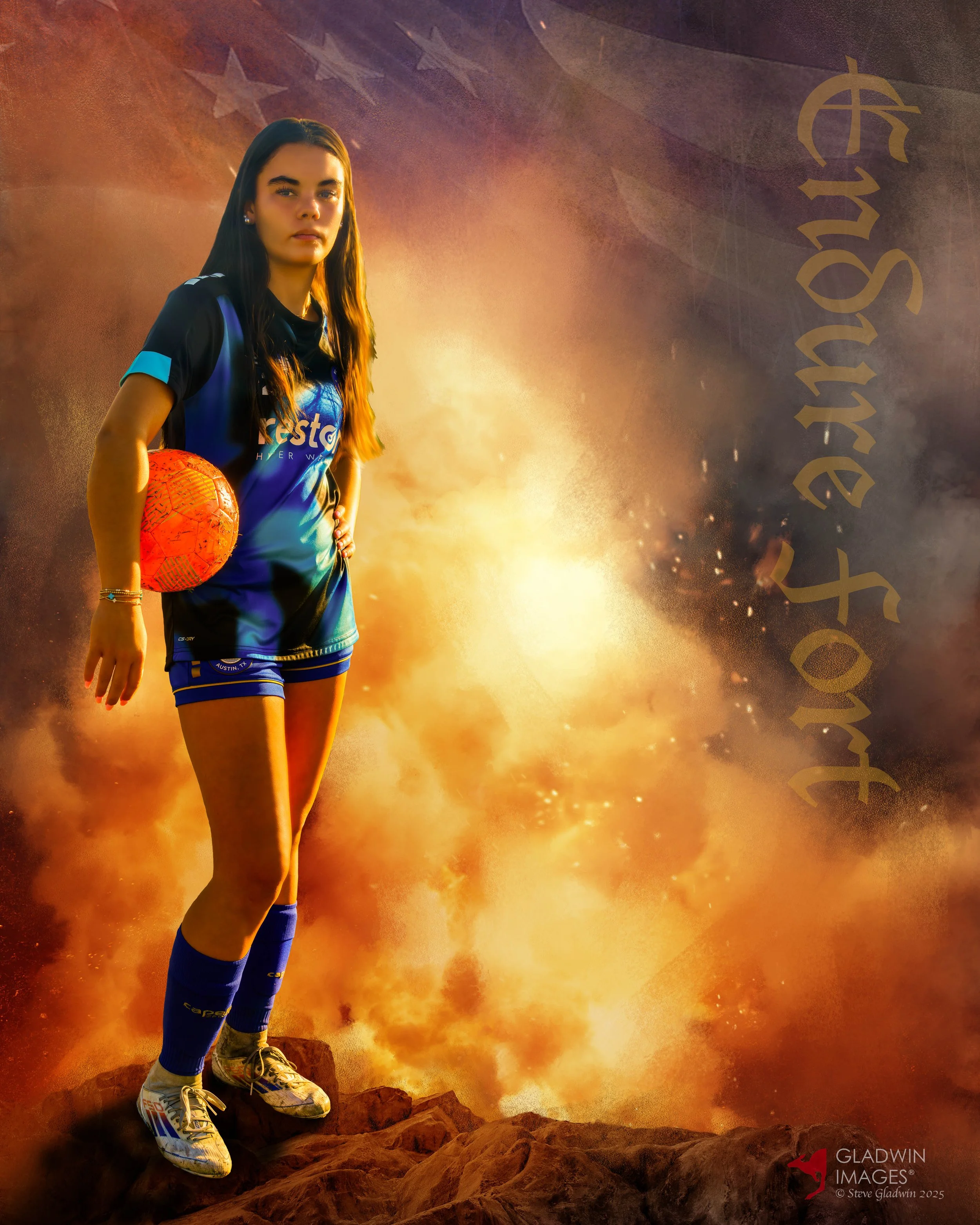 A girl in a blue sports uniform holding an orange soccer ball, standing on rocks with a fiery, volcanic background and clouds of smoke and ash, with the logo 'Gladwin Images' and the photographer credits in the bottom right corner.