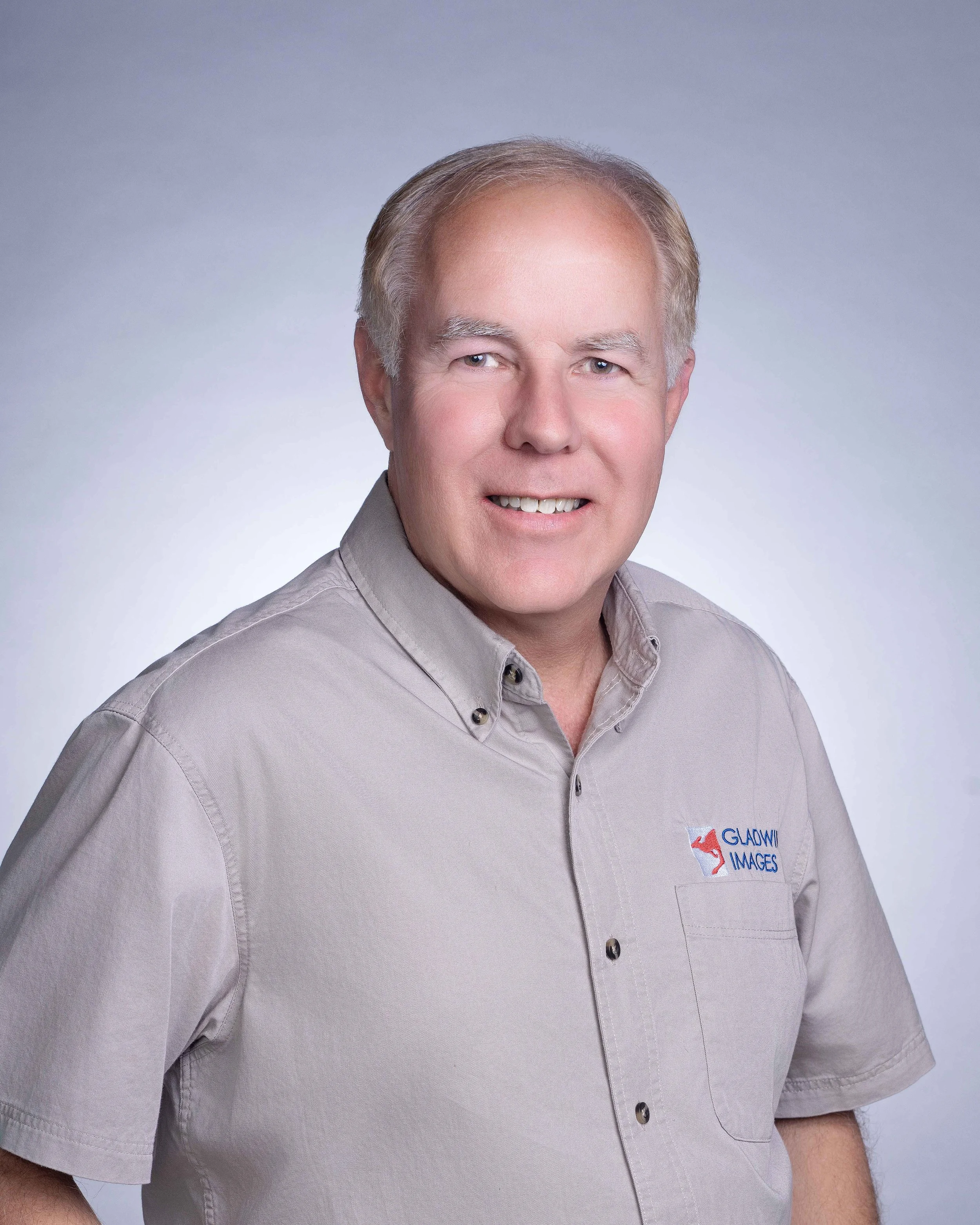 Professional business headshot of a man in a gray shirt against a neutral studio background