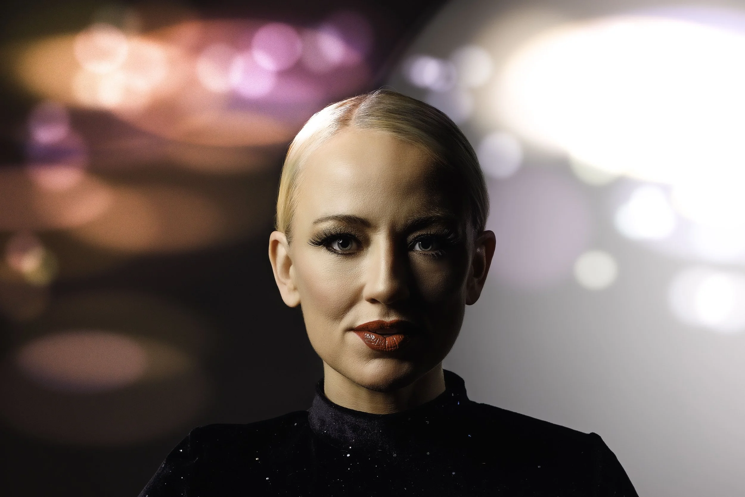 Creative studio portrait of a blonde woman against a colorful blurred-light background