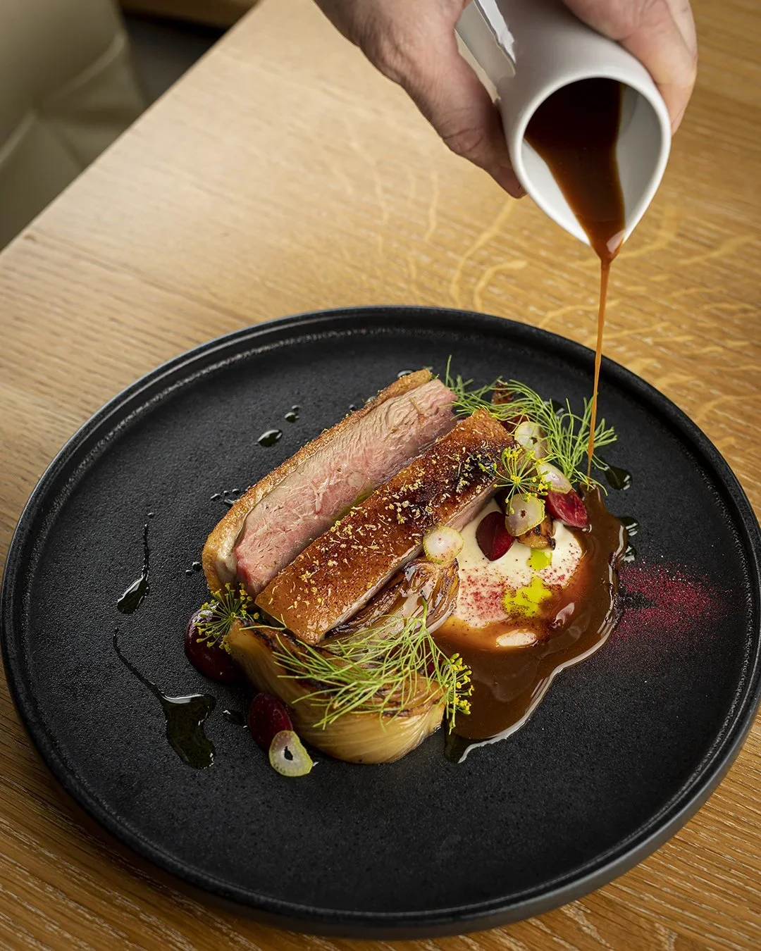 Hand pouring sauce glaze over prepared duck dish