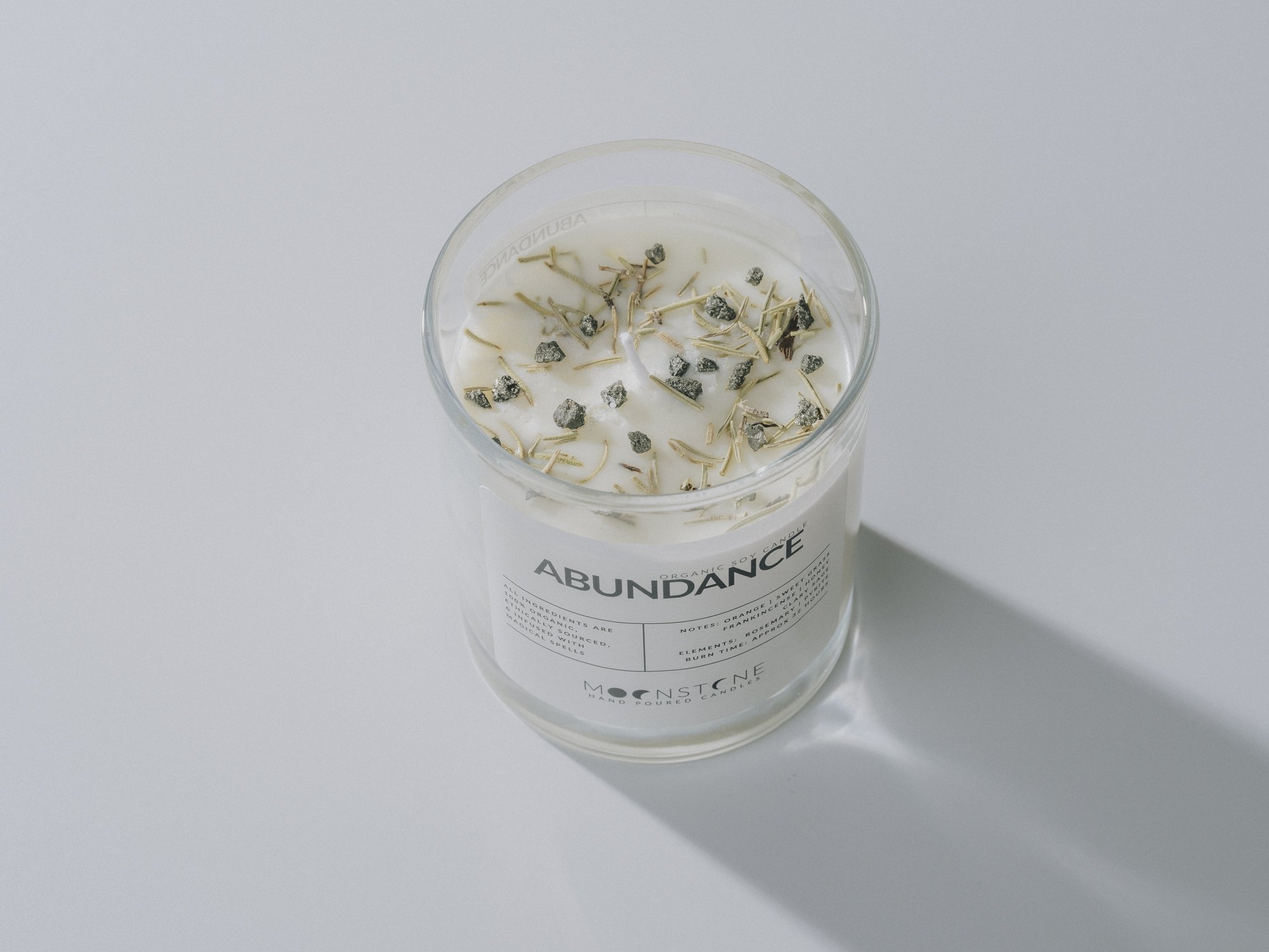 Top angle shot with pyrite stones and rosemary in Moonstone Enchanted Ritual's Abundance Candle