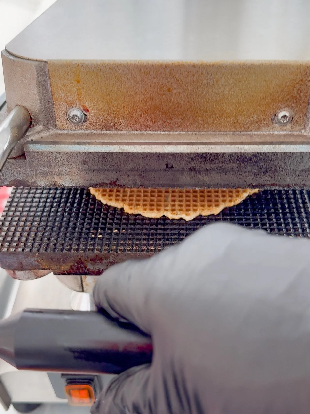 Hands pressing dough in a Dutch stroopwafel iron during a live baking experience